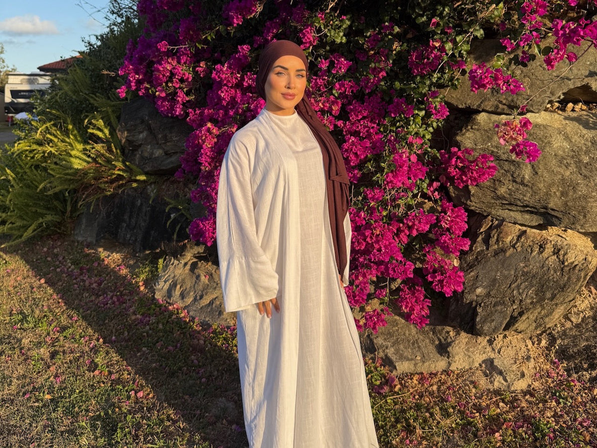 linen abaya worned by model woman with pink purple flowers in the back the fajr sun is glowing on her