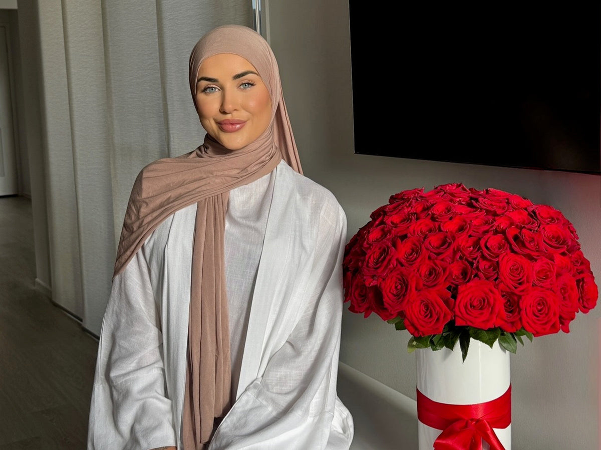 model woman posing with neutral tone hijab and white linen abaya made from organic cotton and linen next to red roses. beautiful aesthetic look