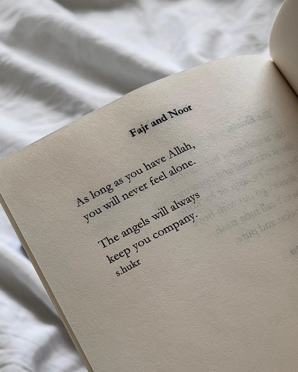 An open book lying on white fabric, showing a printed quote titled 'Fajr and Noor' with the text, 'As long as you have Allah, you will never feel alone. The angels will always keep you company.