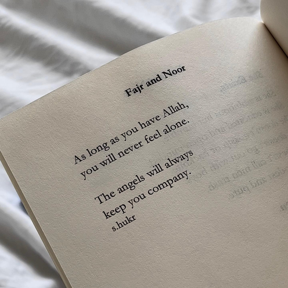 An open book showing a printed poem titled 'Fajr and Noor' on warm cream-colored pages, photographed against soft white fabric.