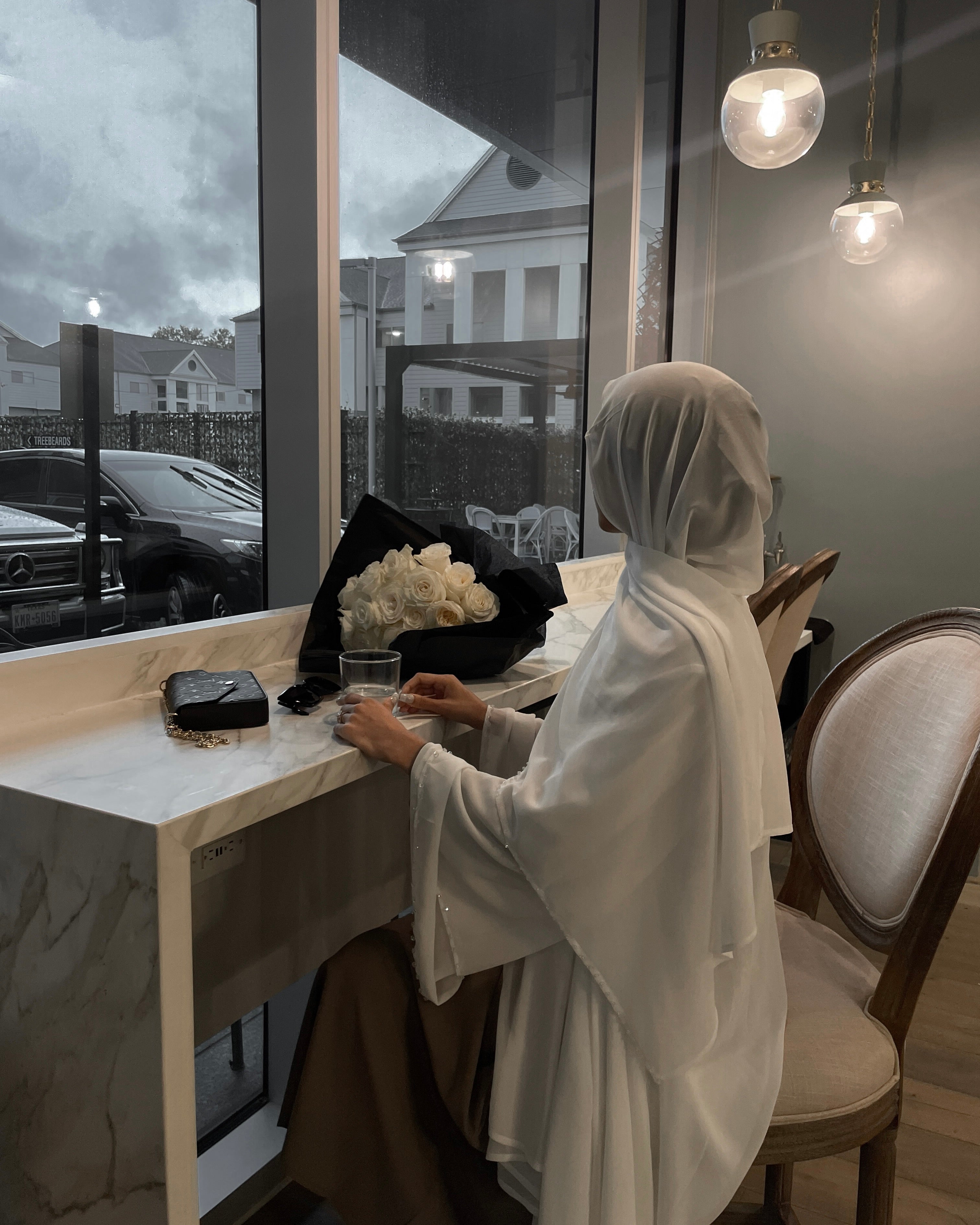 Person in a white hijab sitting at a desk with a laptop, surrounded by decor elements.