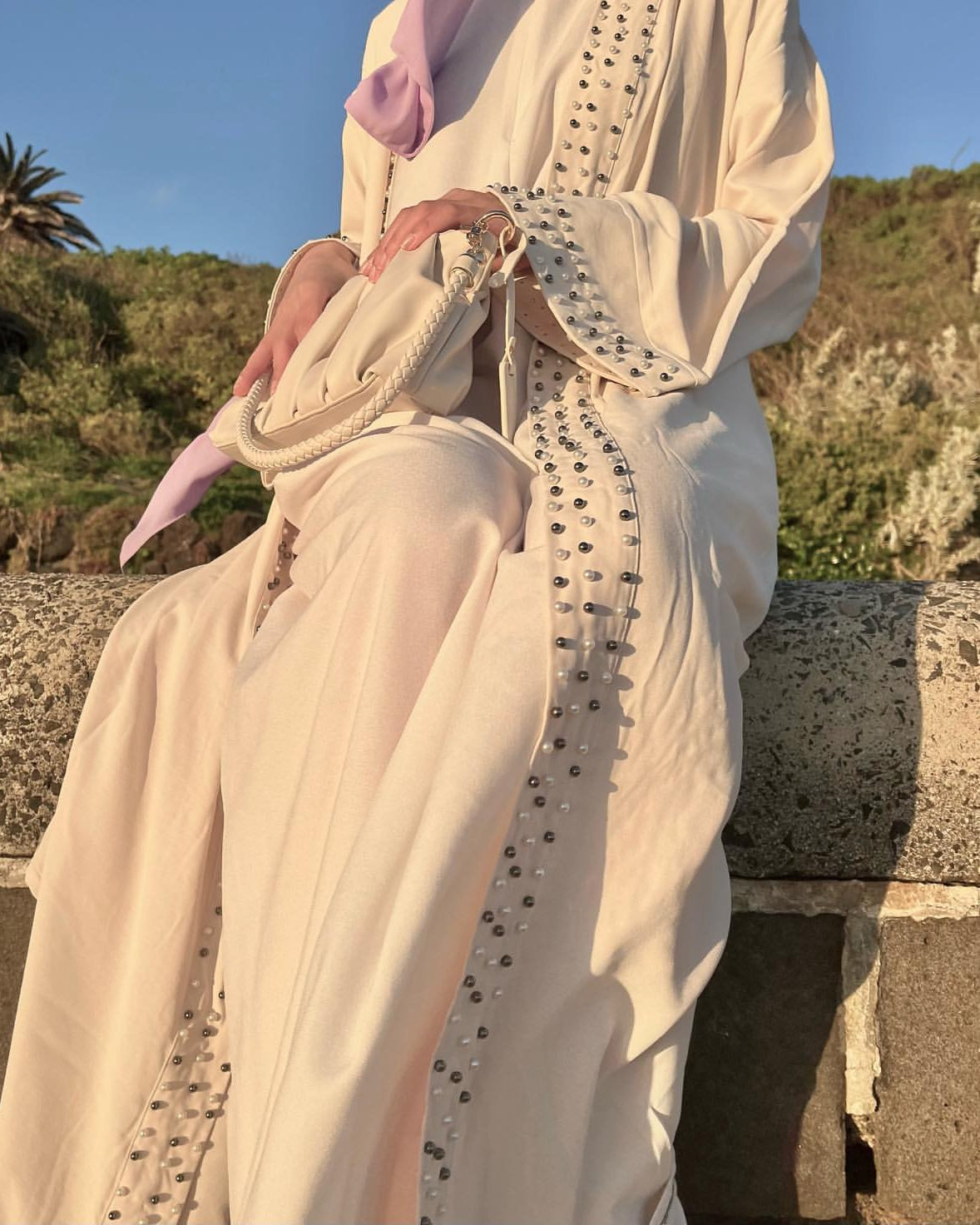Person wearing a light-colored dress with intricate detailing in an outdoor setting.