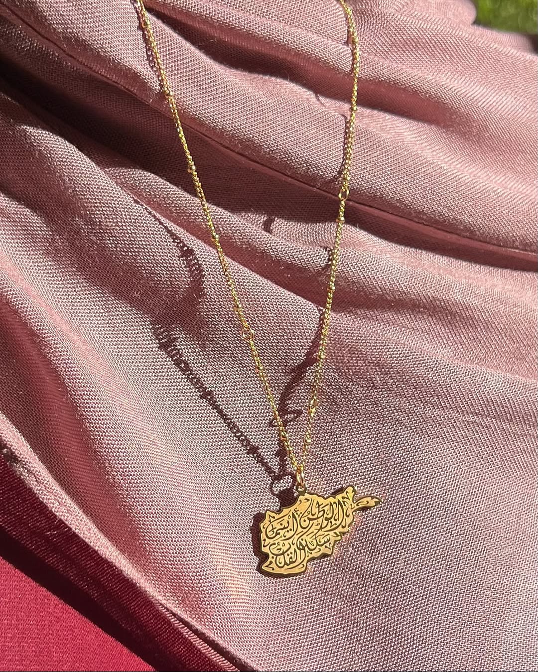 Gold Afghanistan necklace with a pendant on a pink fabric background