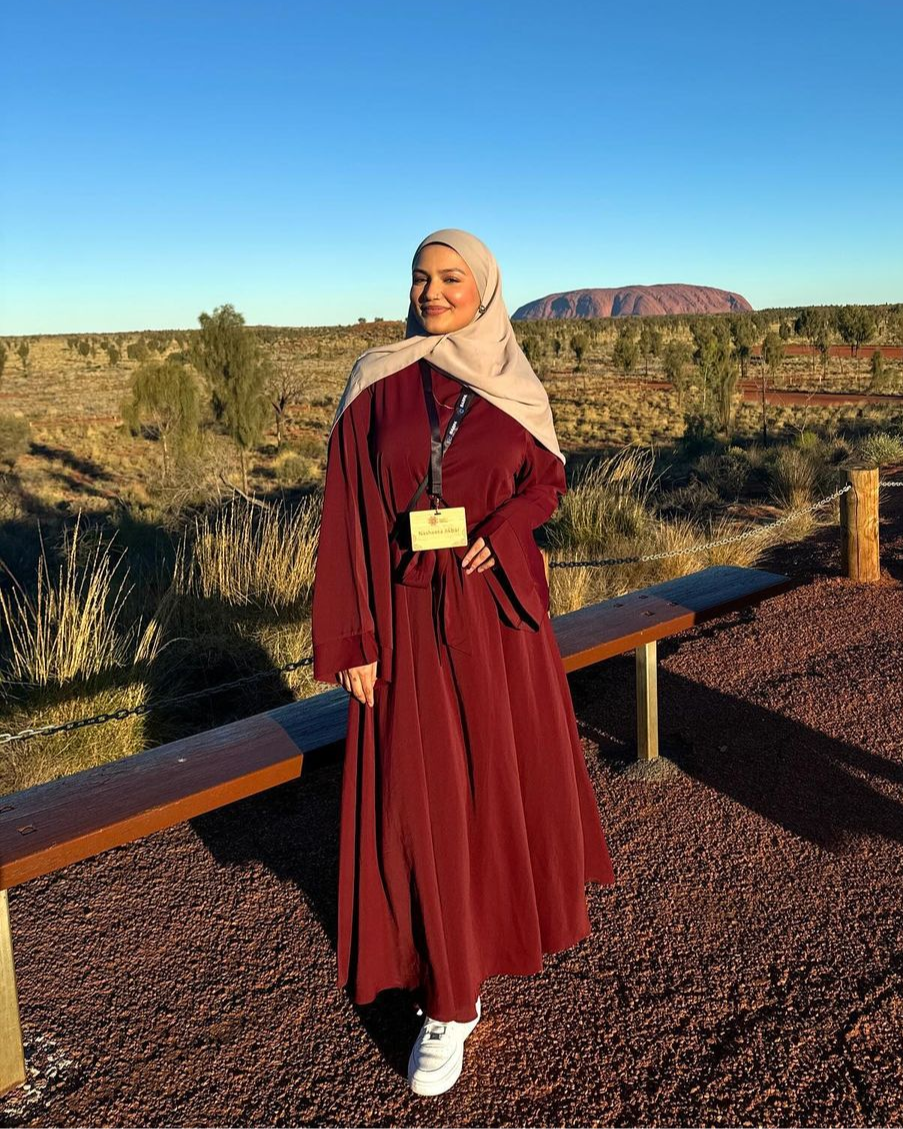 Woman in a red dress and beige hijab standing in front of Uluru, Australia.