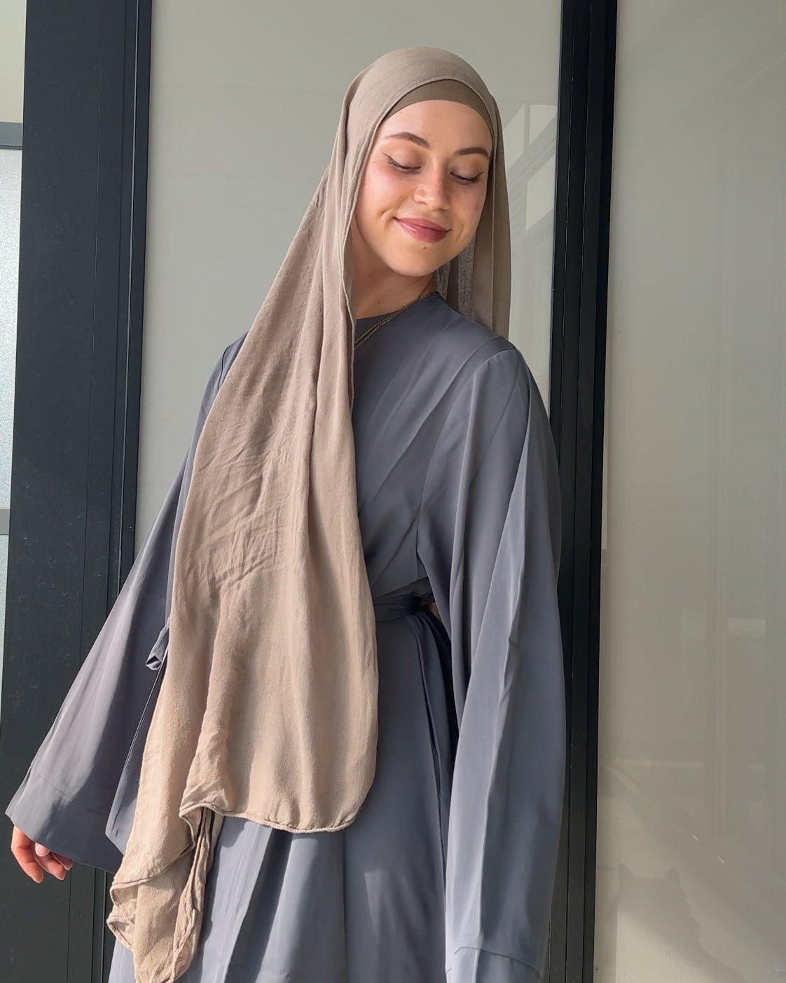Woman wearing a beige hijab and gray outfit against a neutral background