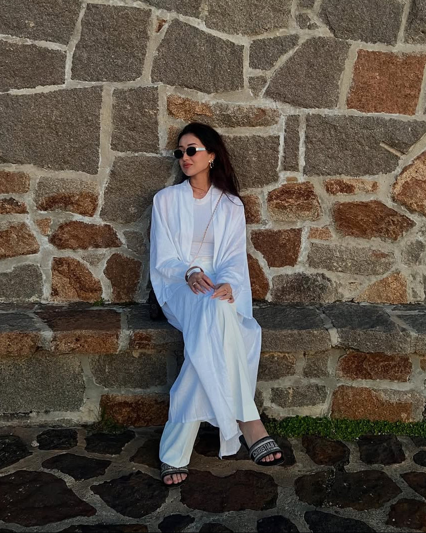 Person in white outfit sitting against a stone wall