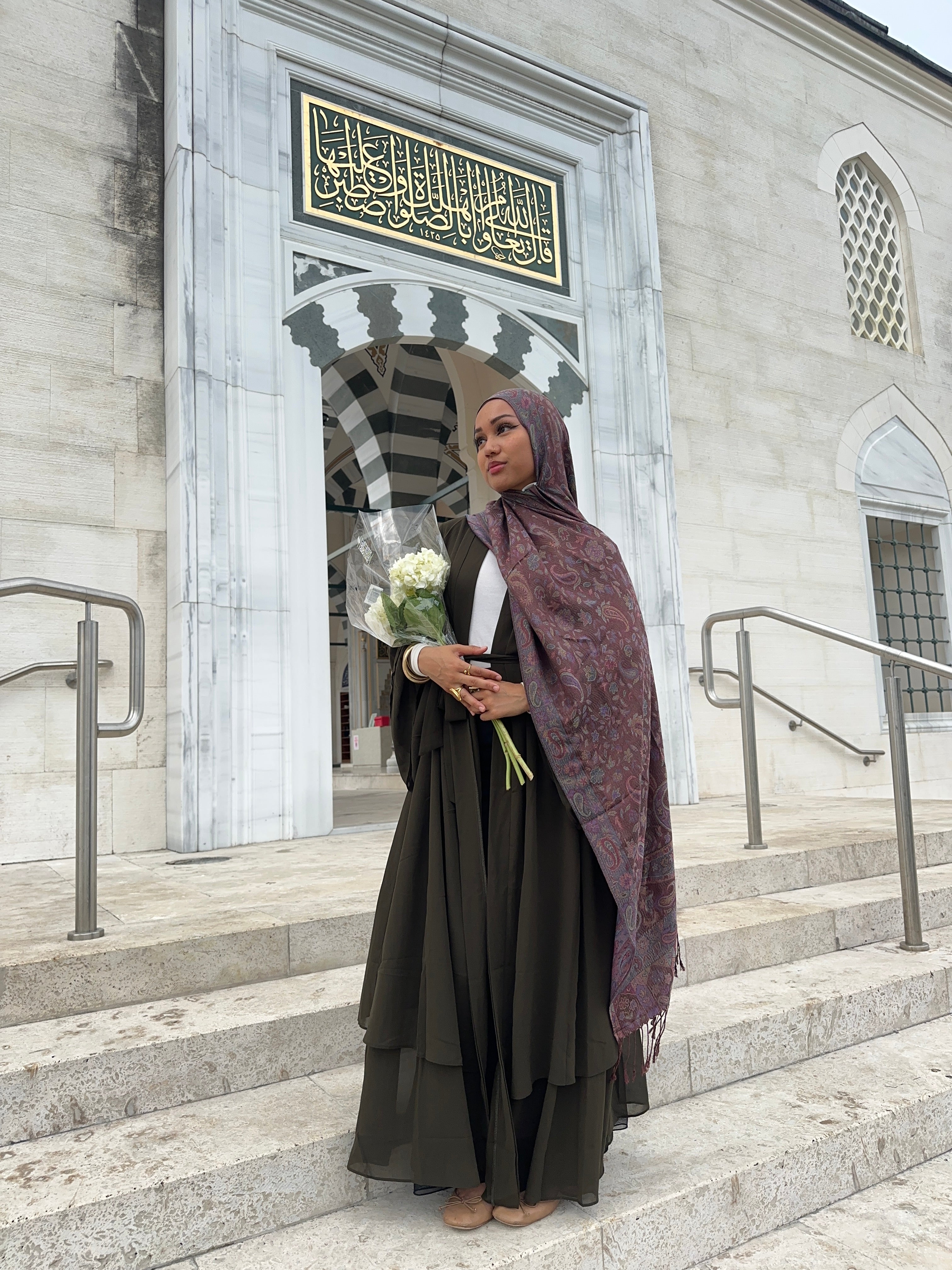 Person holding flowers standing in front of a building entrance with decorative elements.
