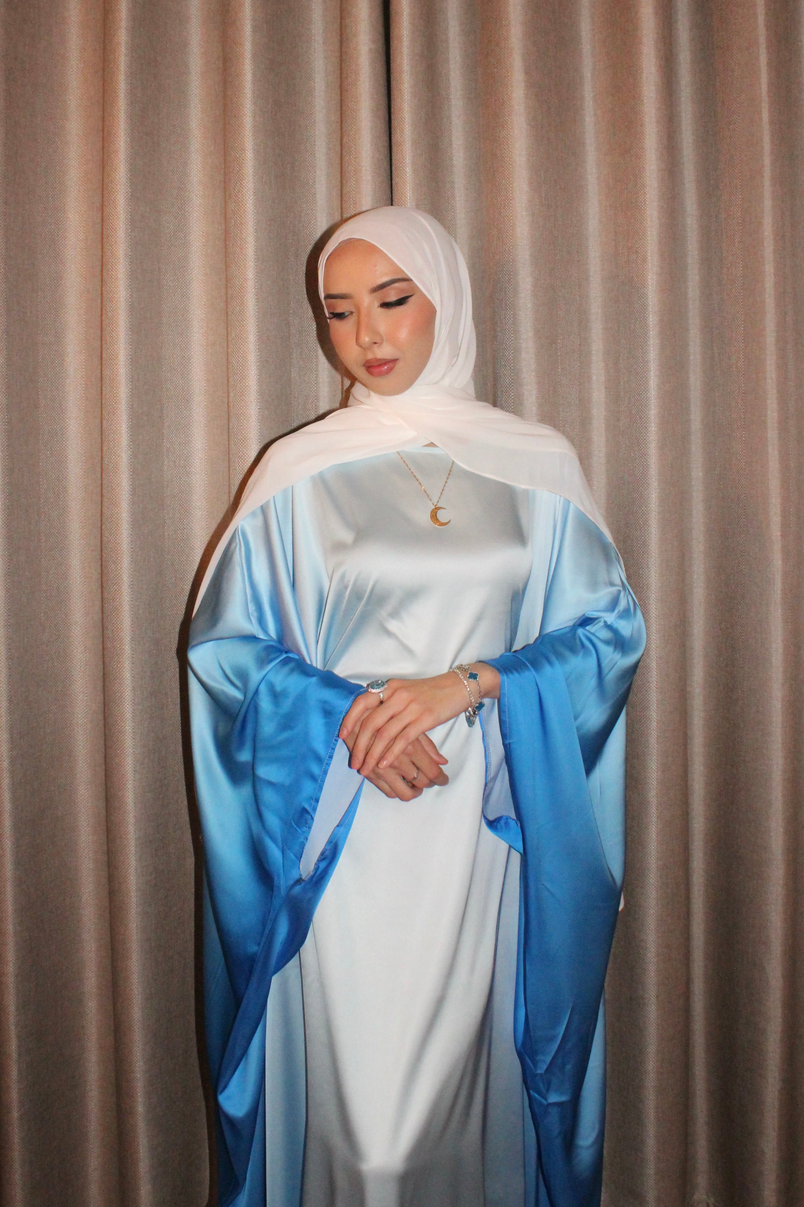 Woman wearing a white and blue dress against a beige curtain background