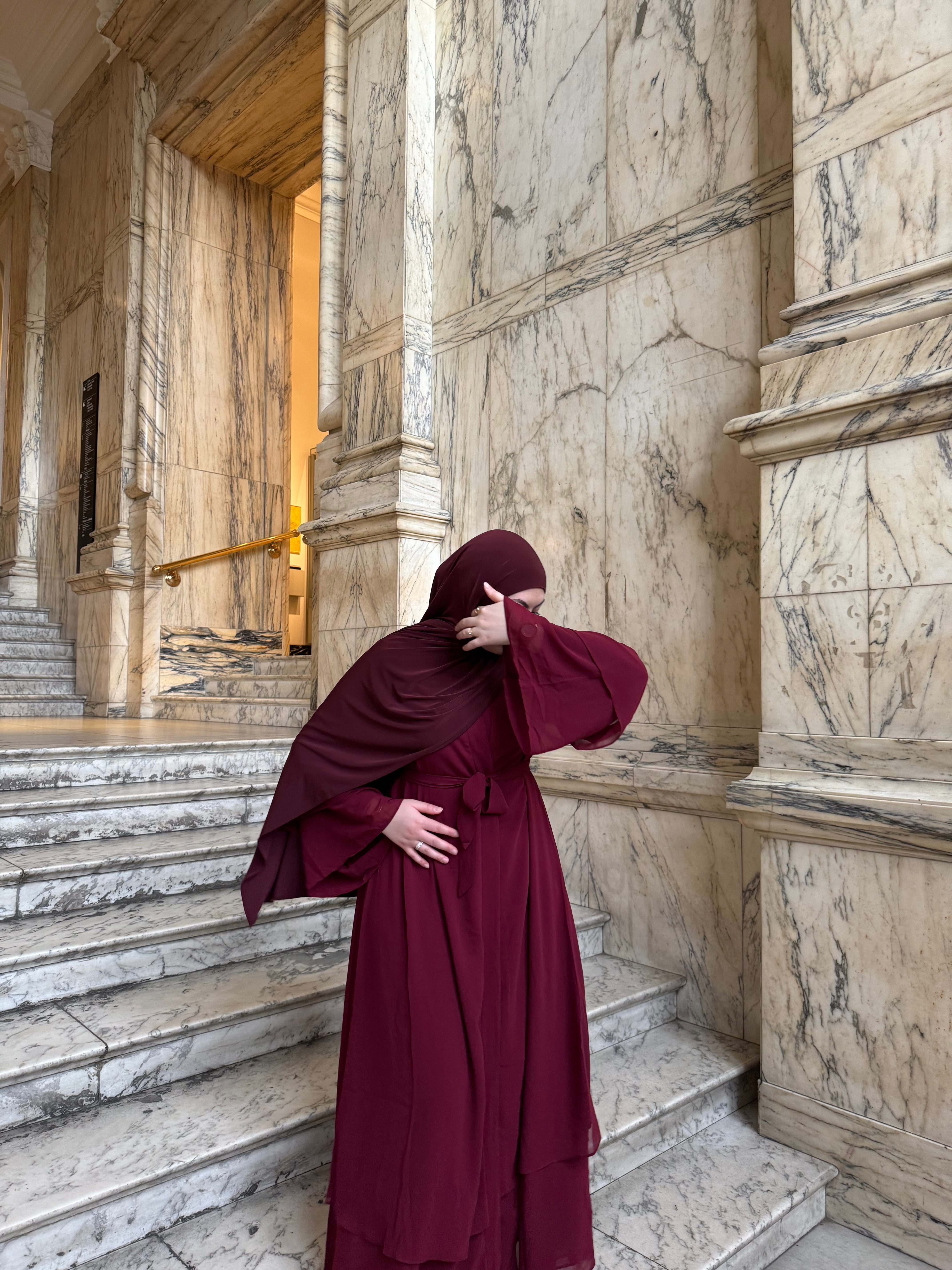 Person in a burgundy dress standing on marble steps with a marble wall in the background