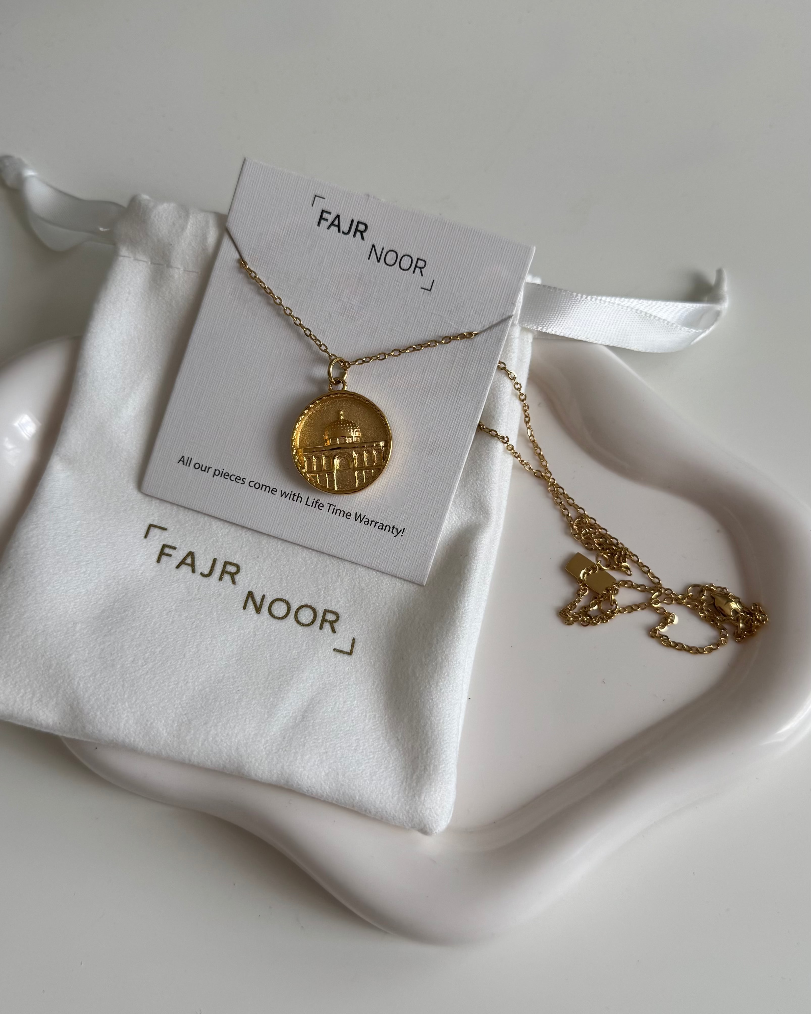 Gold necklace on a white stand with 'FAJR NOOR' branding