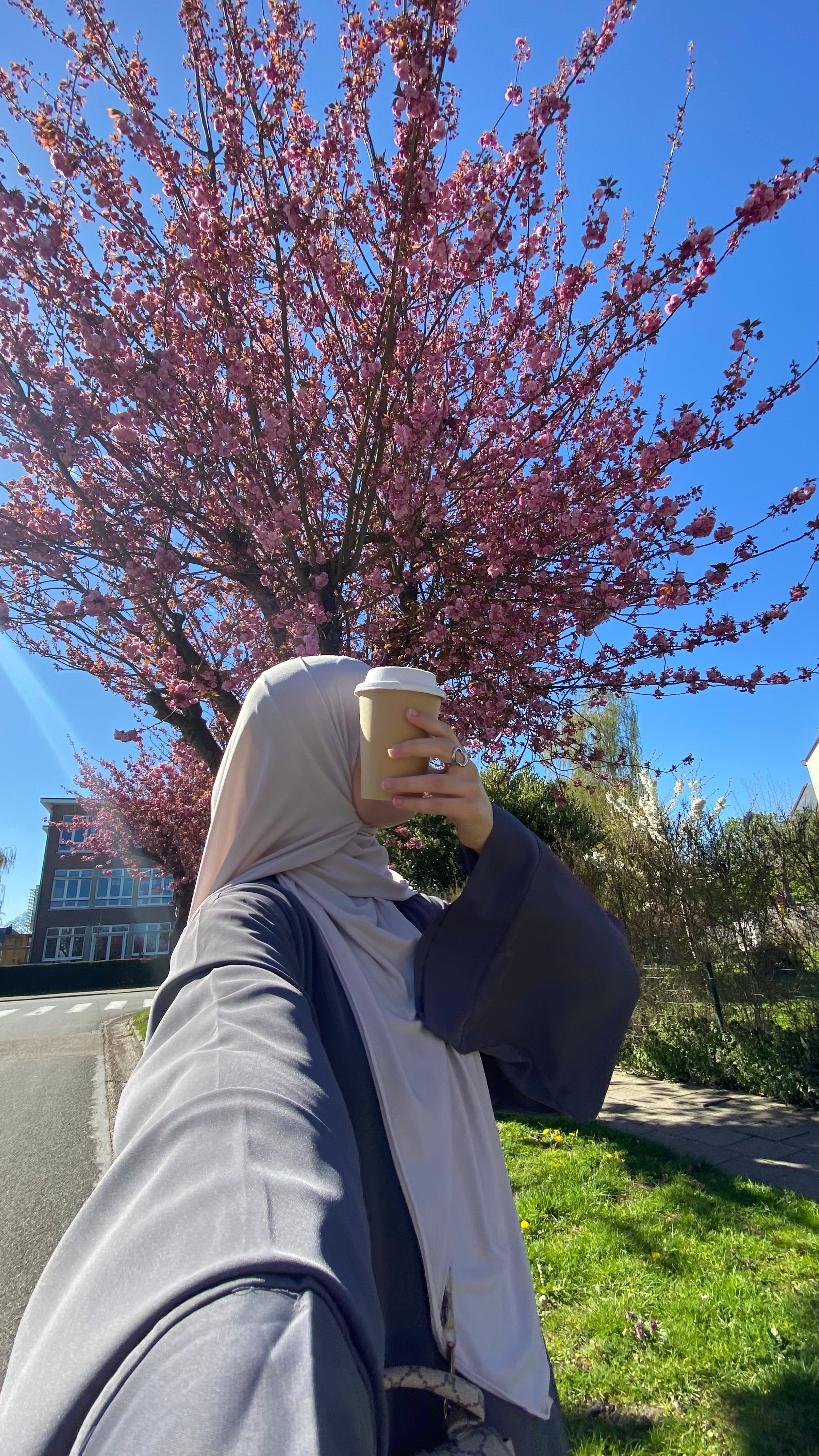 Hijab wearing muslim woman in charcoal abaya taking a selfie with cherry blossoms in the background