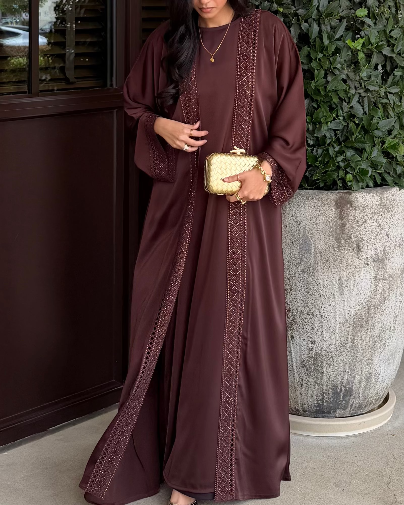 Woman wearing a long brown dress with intricate patterns, standing outdoors.