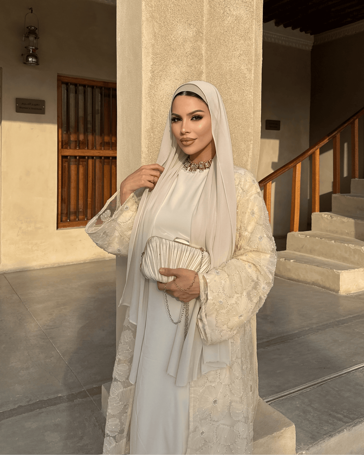 Woman in a white traditional outfit standing in front of a building entrance.