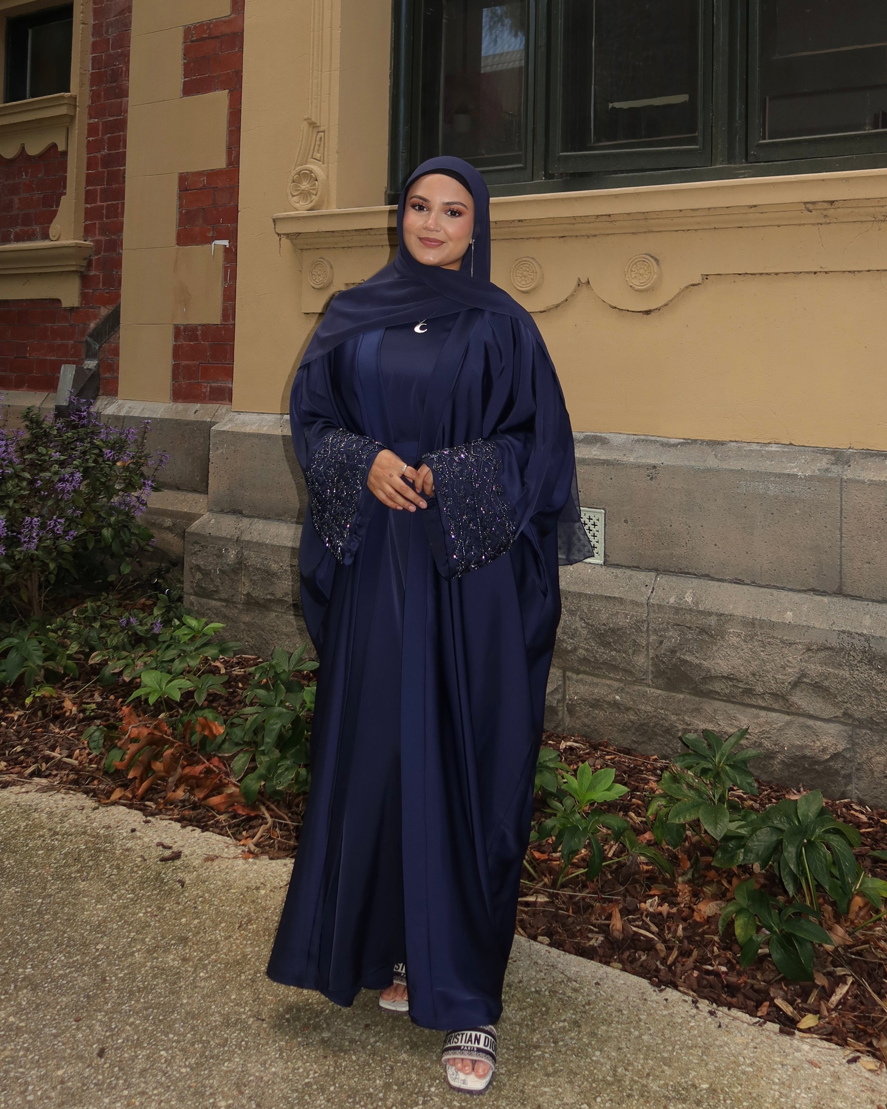 Woman in a dark blue dress standing in front of a building with decorative architecture.
