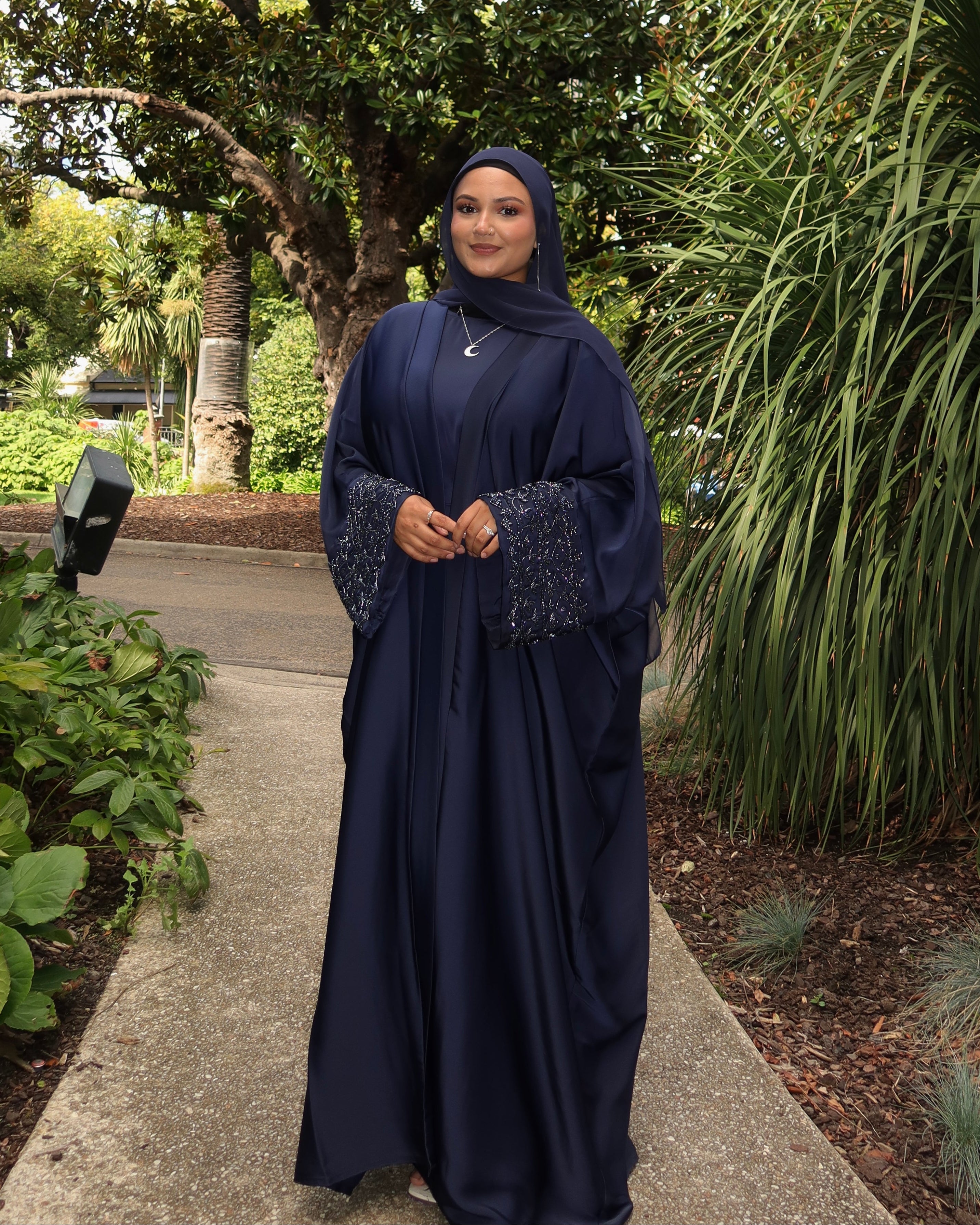 Woman in a navy abaya standing on a path with greenery around