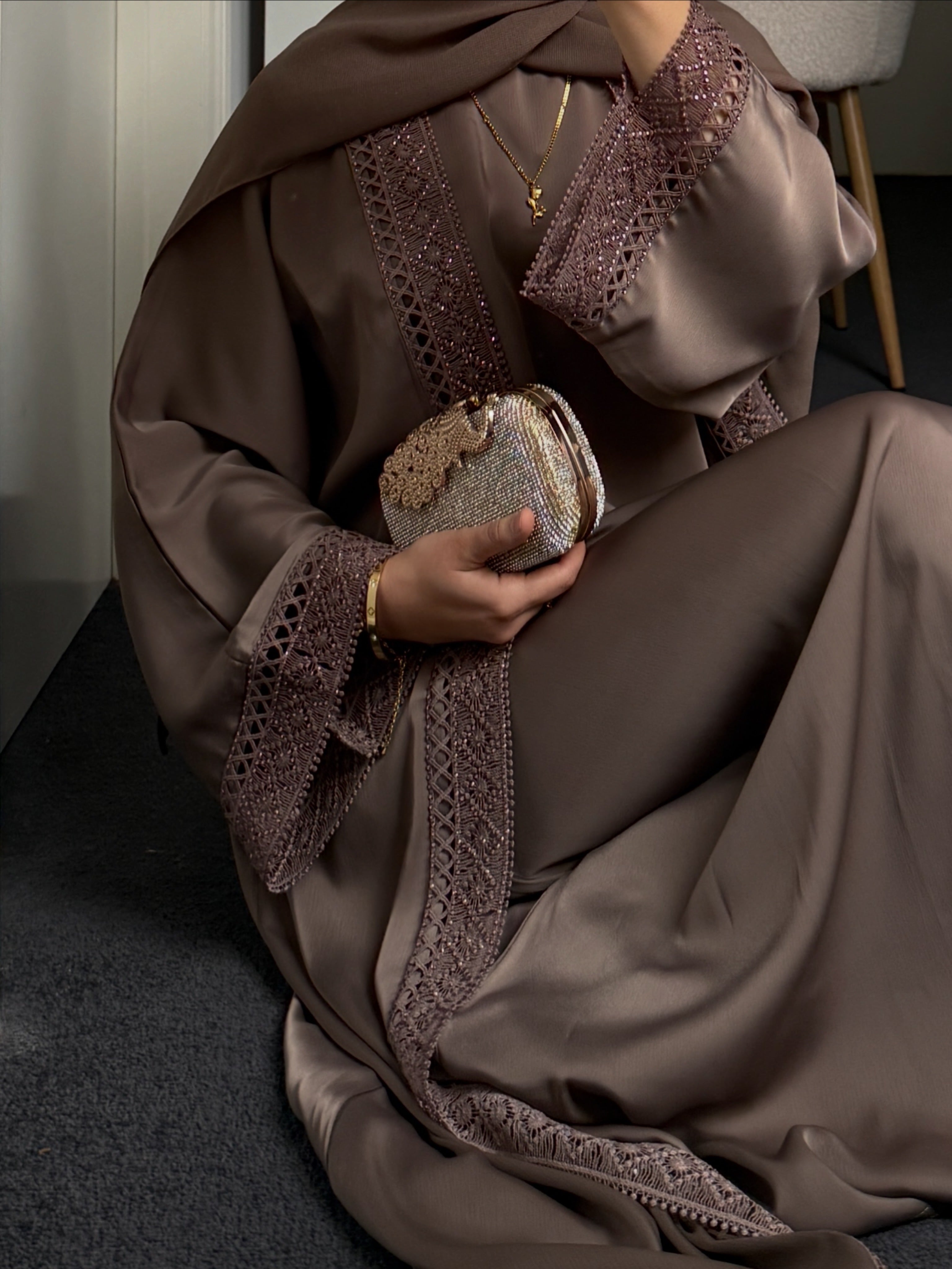 Person wearing a mocha abaya with intricate lace details, holding a matching clutch.