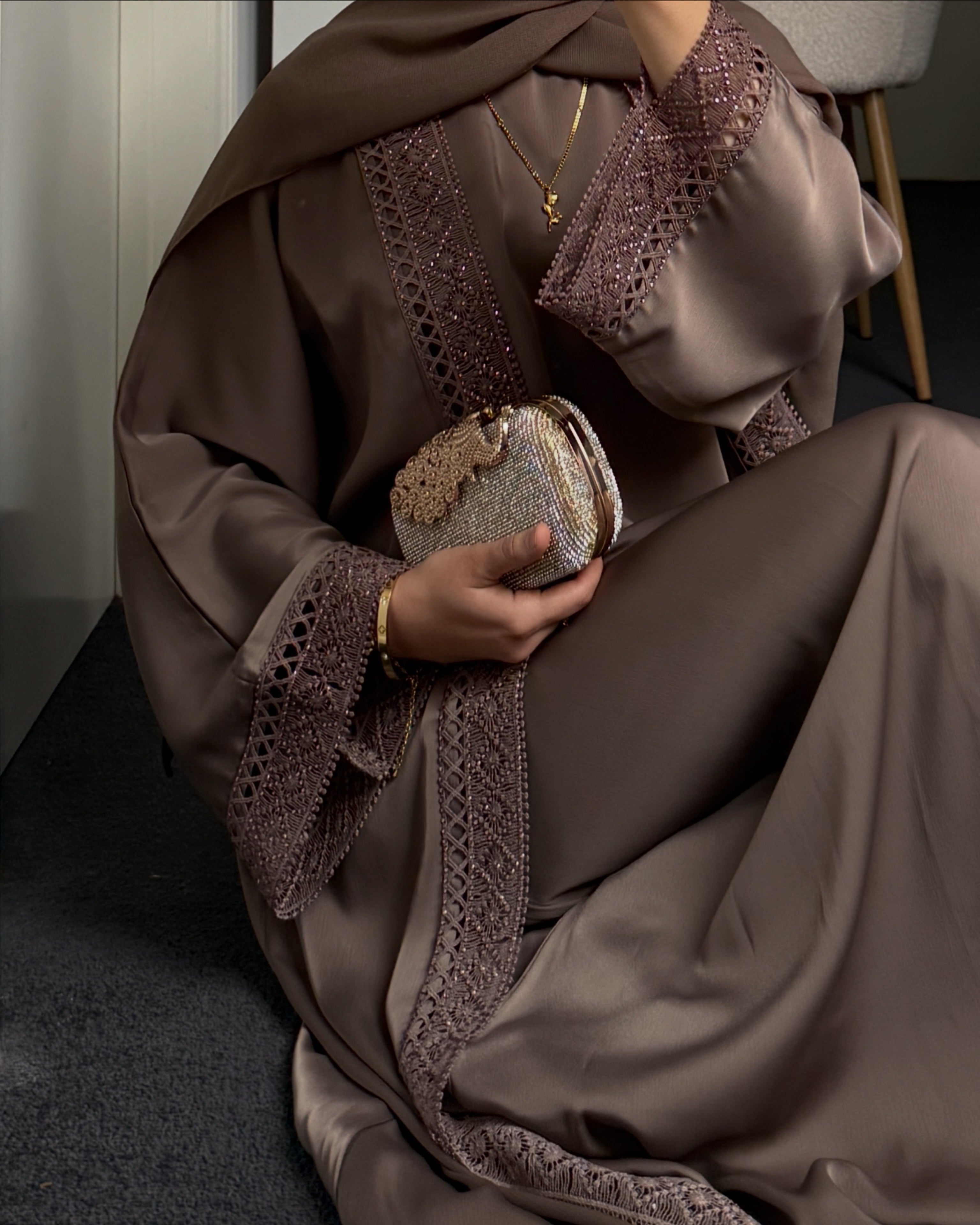 Person wearing a mocha abaya with intricate lace details, holding a matching clutch.