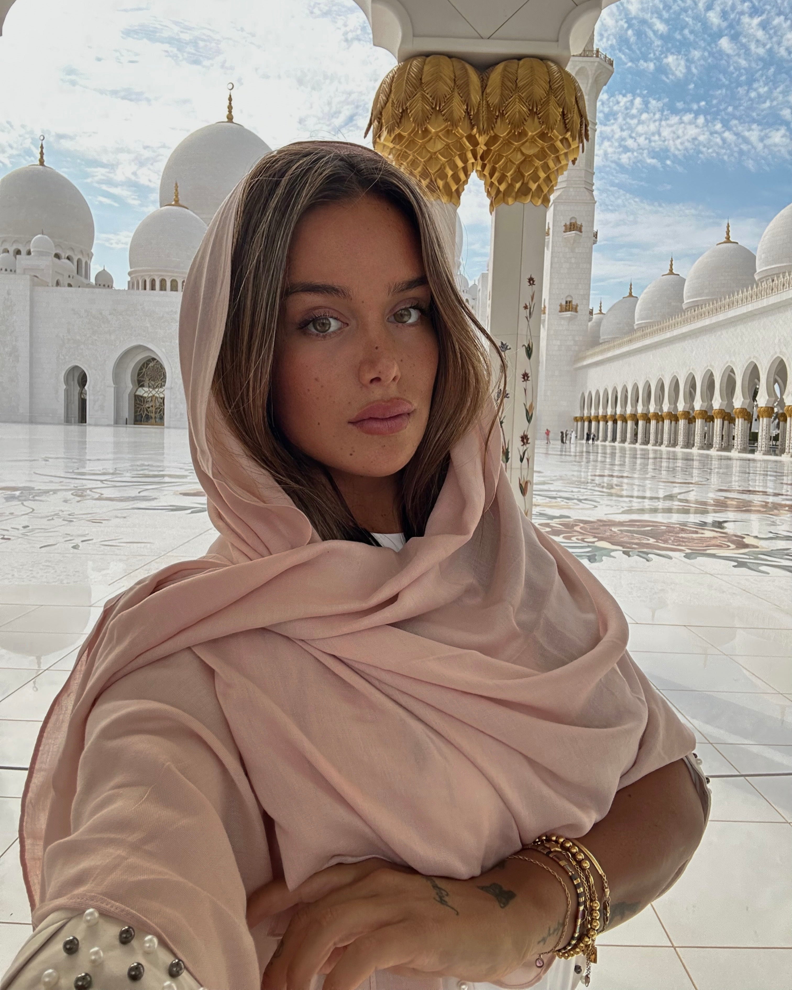 Woman in a pink hijab standing in a mosque courtyard.
