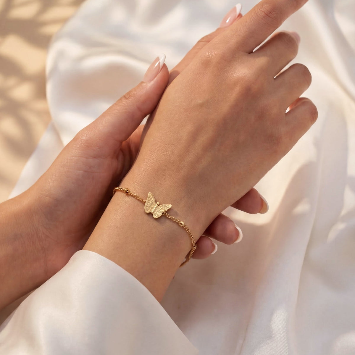 Gold butterfly bracelet on a hand with a soft white background