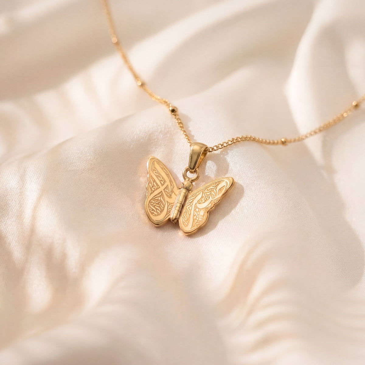 Gold butterfly necklace on a soft beige fabric background