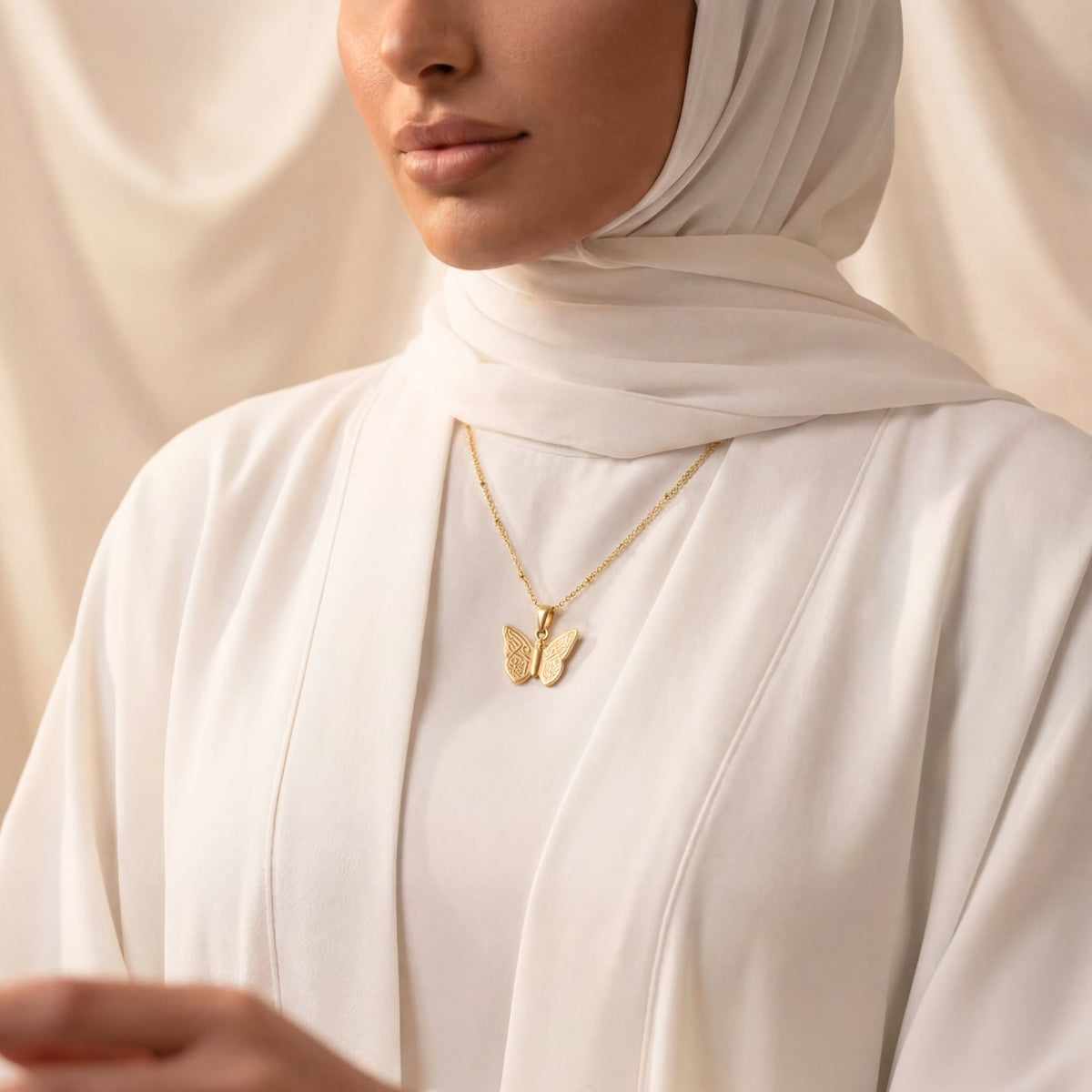 Woman wearing a gold butterfly necklace against a beige background