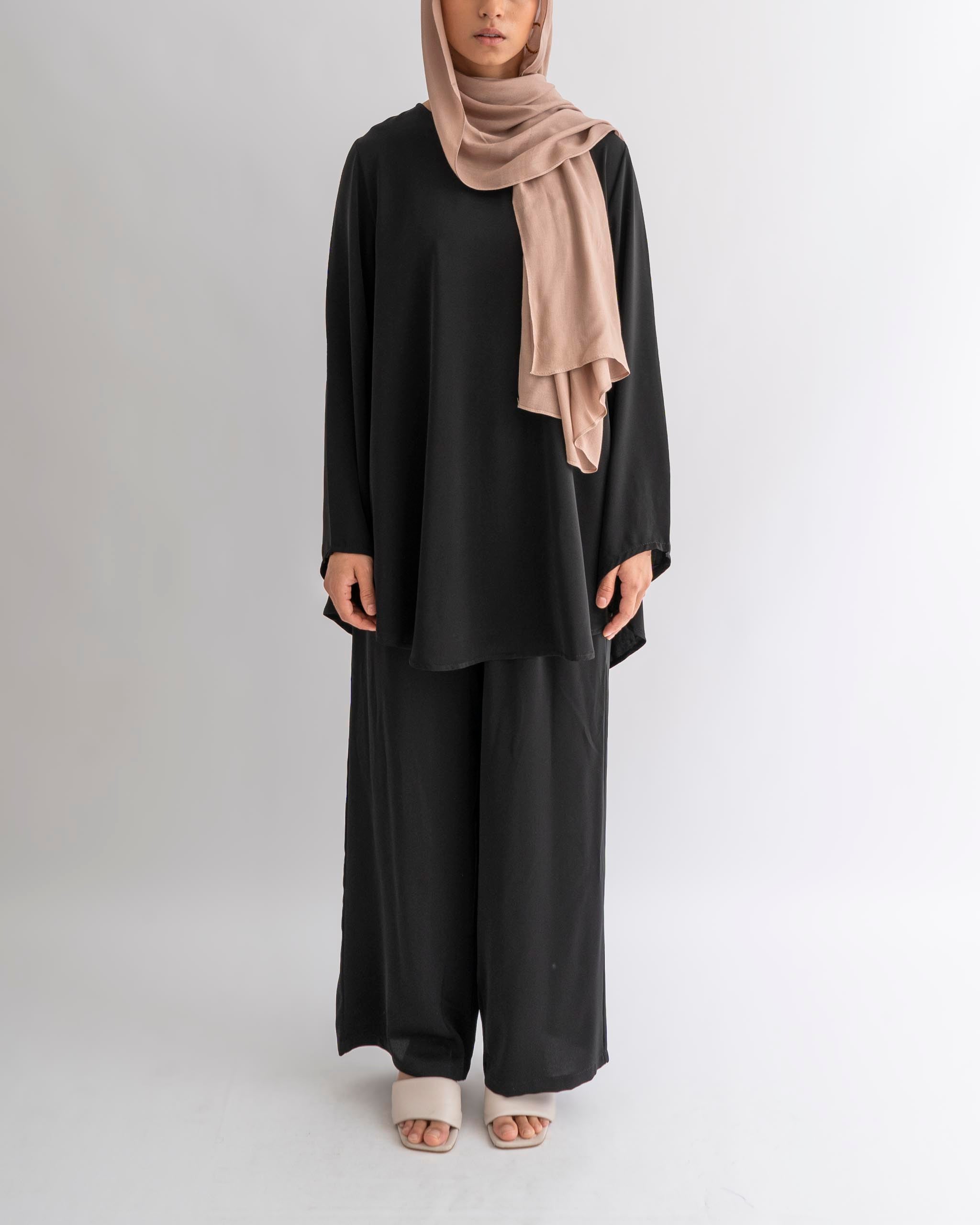 A model wearing a black modest casual loungewear set with a matching top and wide trousers, including a belt, standing against a white background.