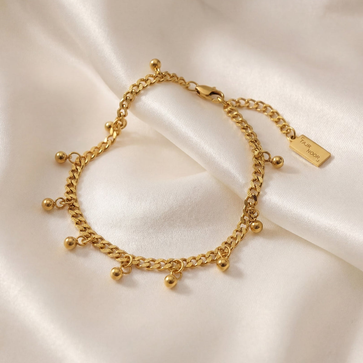 Gold bracelet with small beads on a white satin background