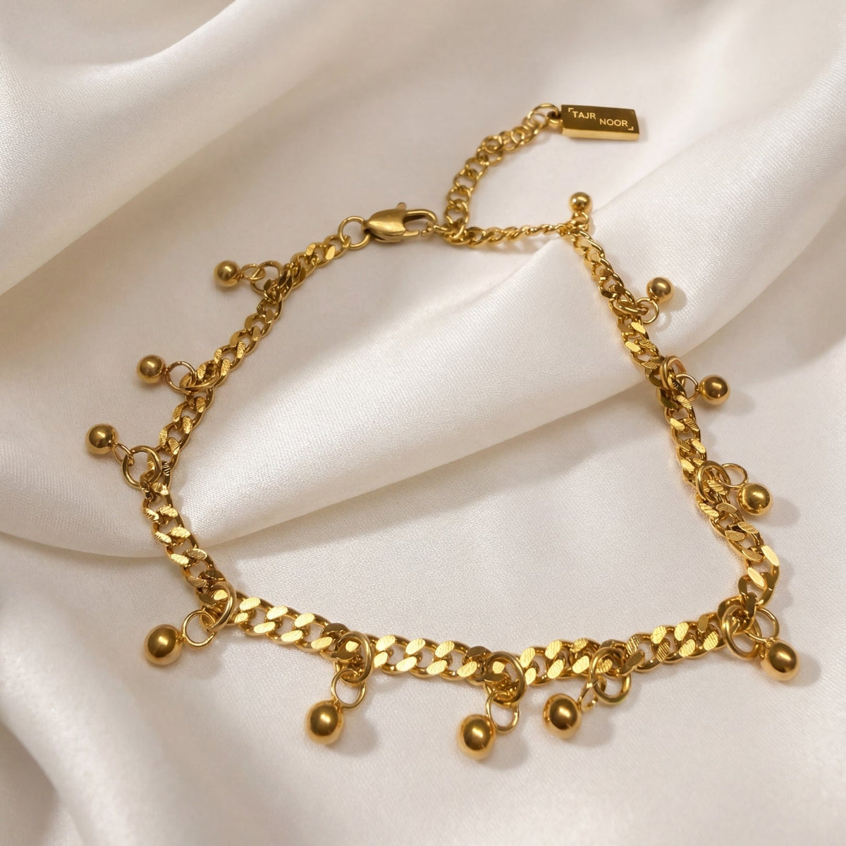 Gold bracelet with spherical charms on a white fabric background