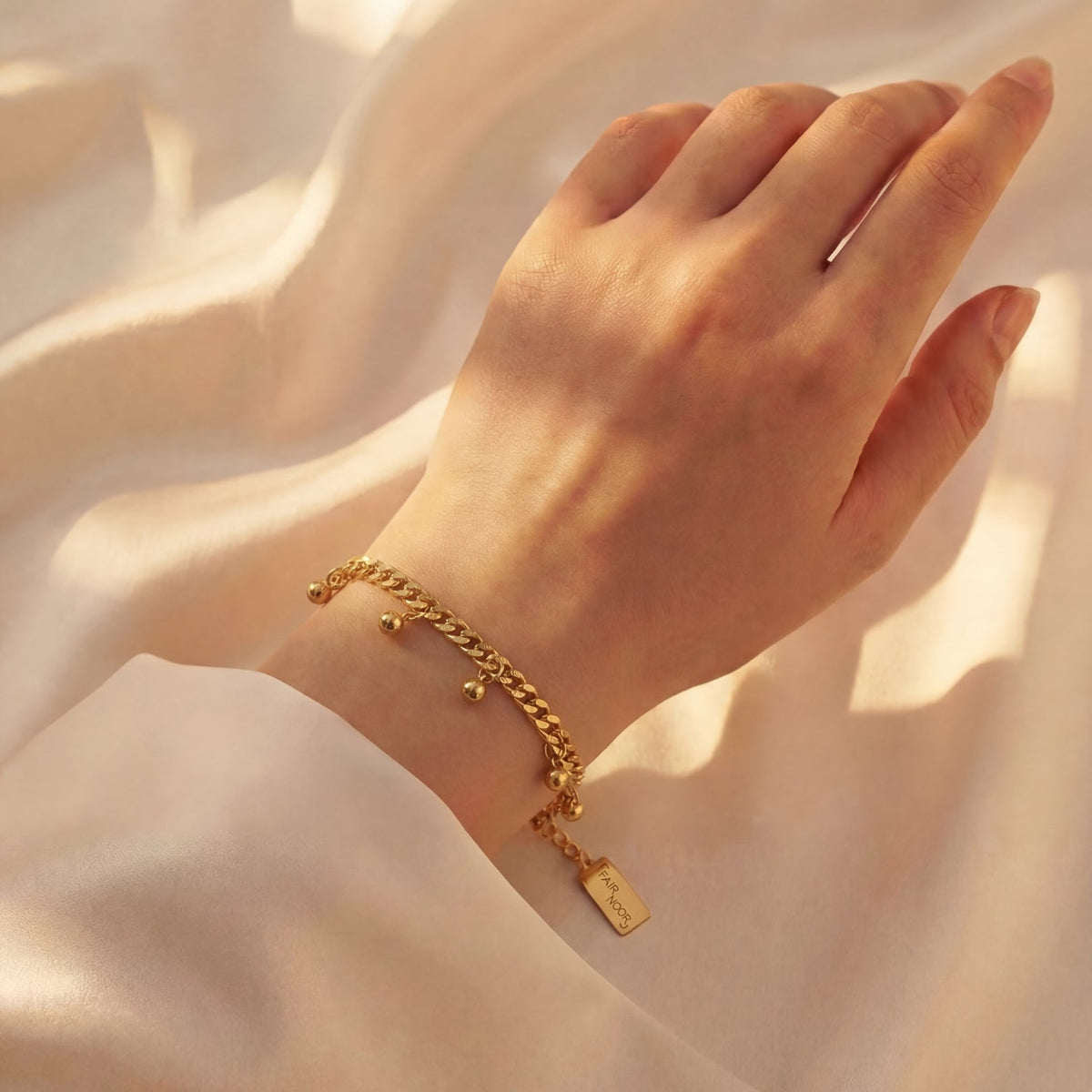 Gold bracelet with a tag on a hand against a soft beige background