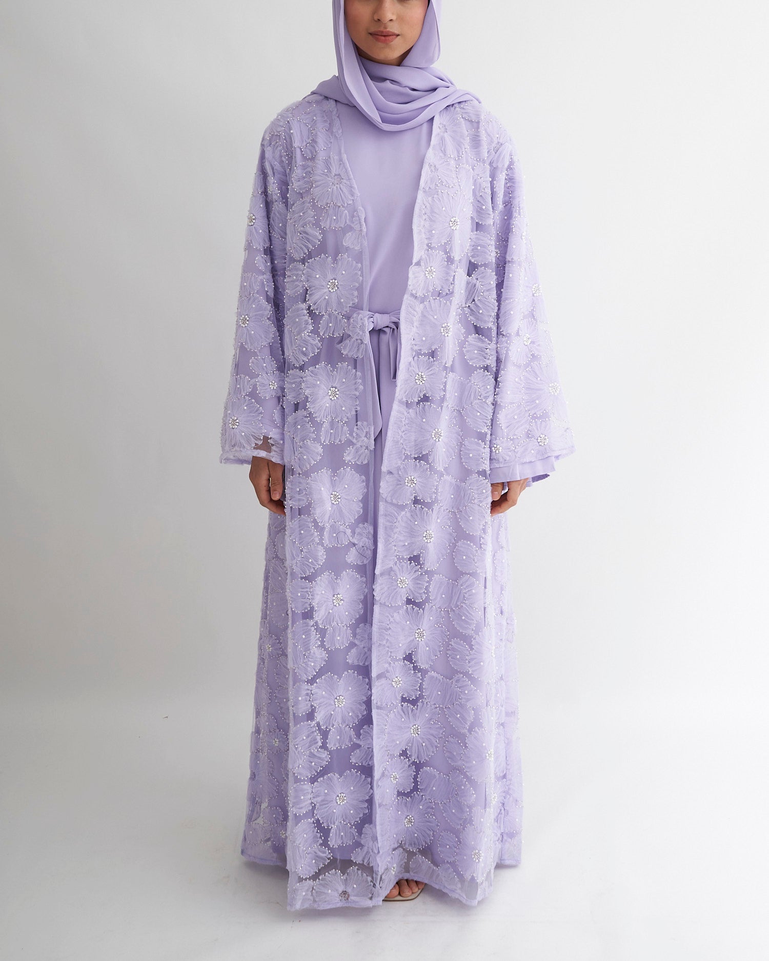 Person wearing a light purple floral dress and hijab on a white background