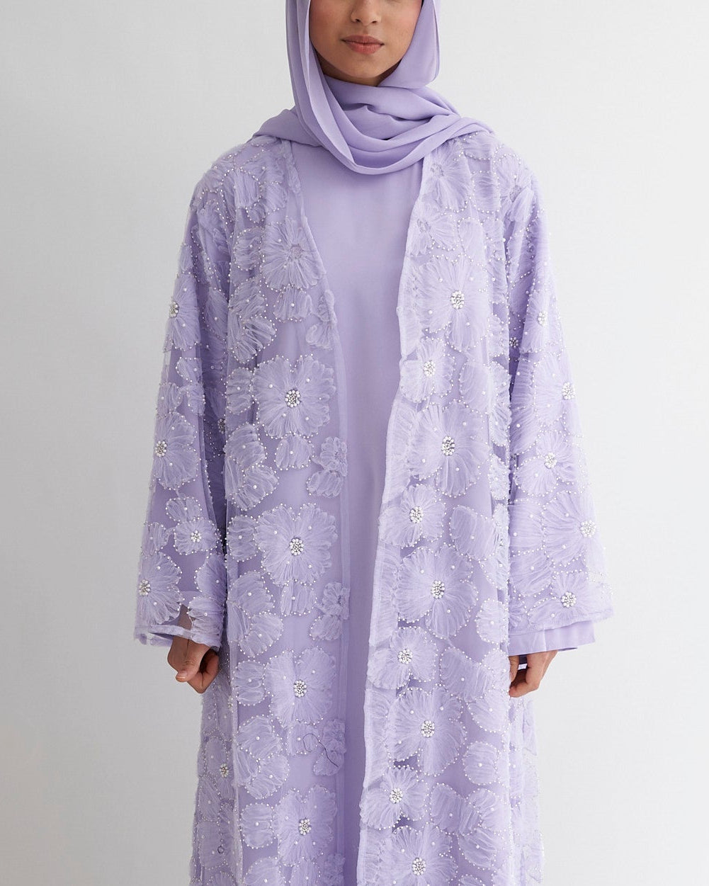 Person wearing a long, light purple dress with a matching hijab on a white background