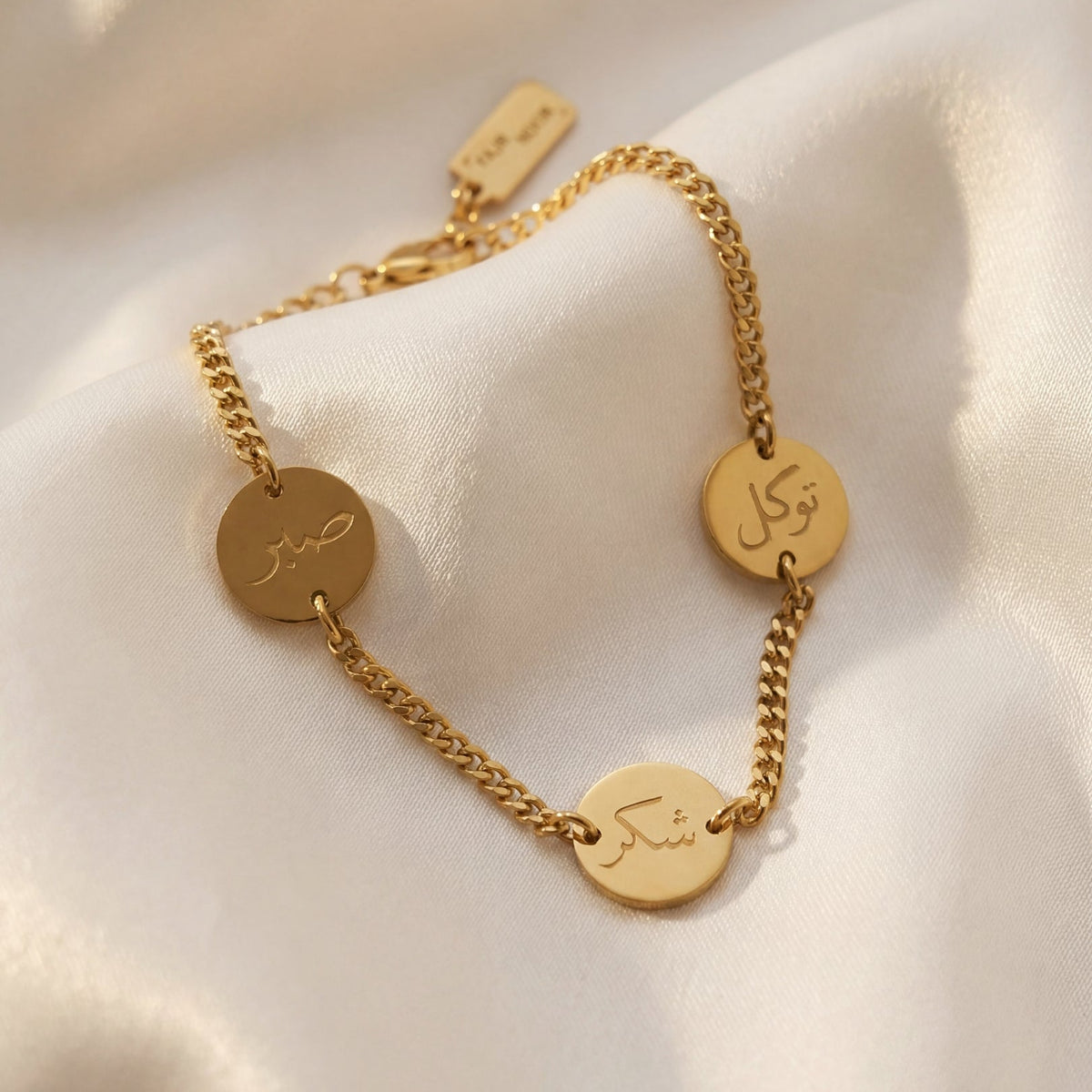 Gold bracelet with engraved discs on a soft beige fabric background