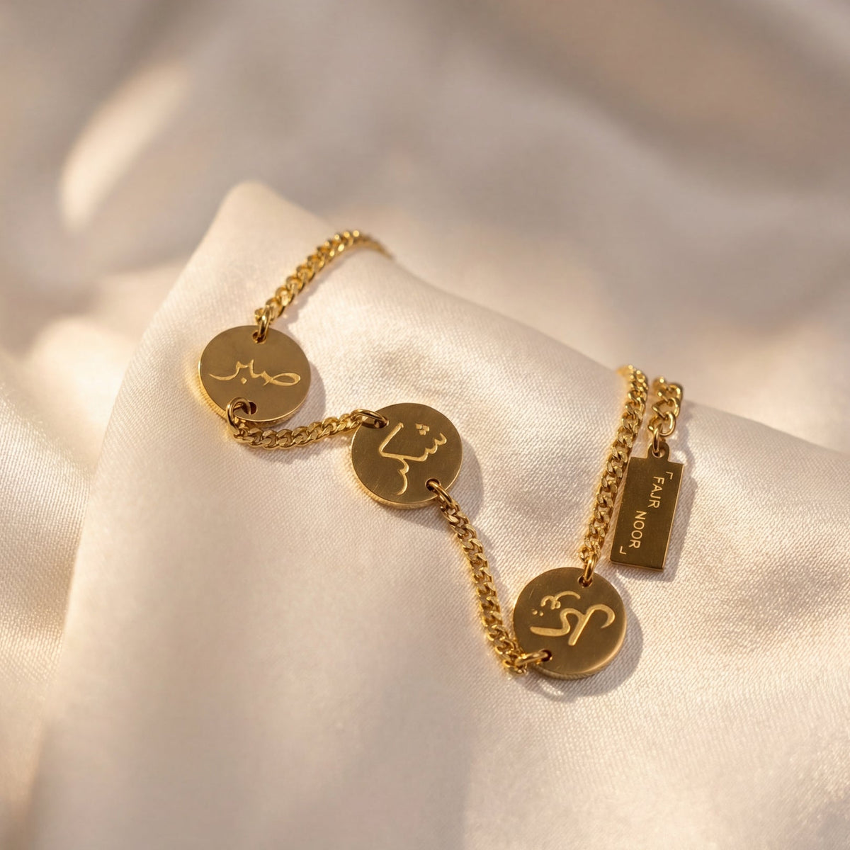 Gold bracelet with engraved charms on a soft beige fabric background