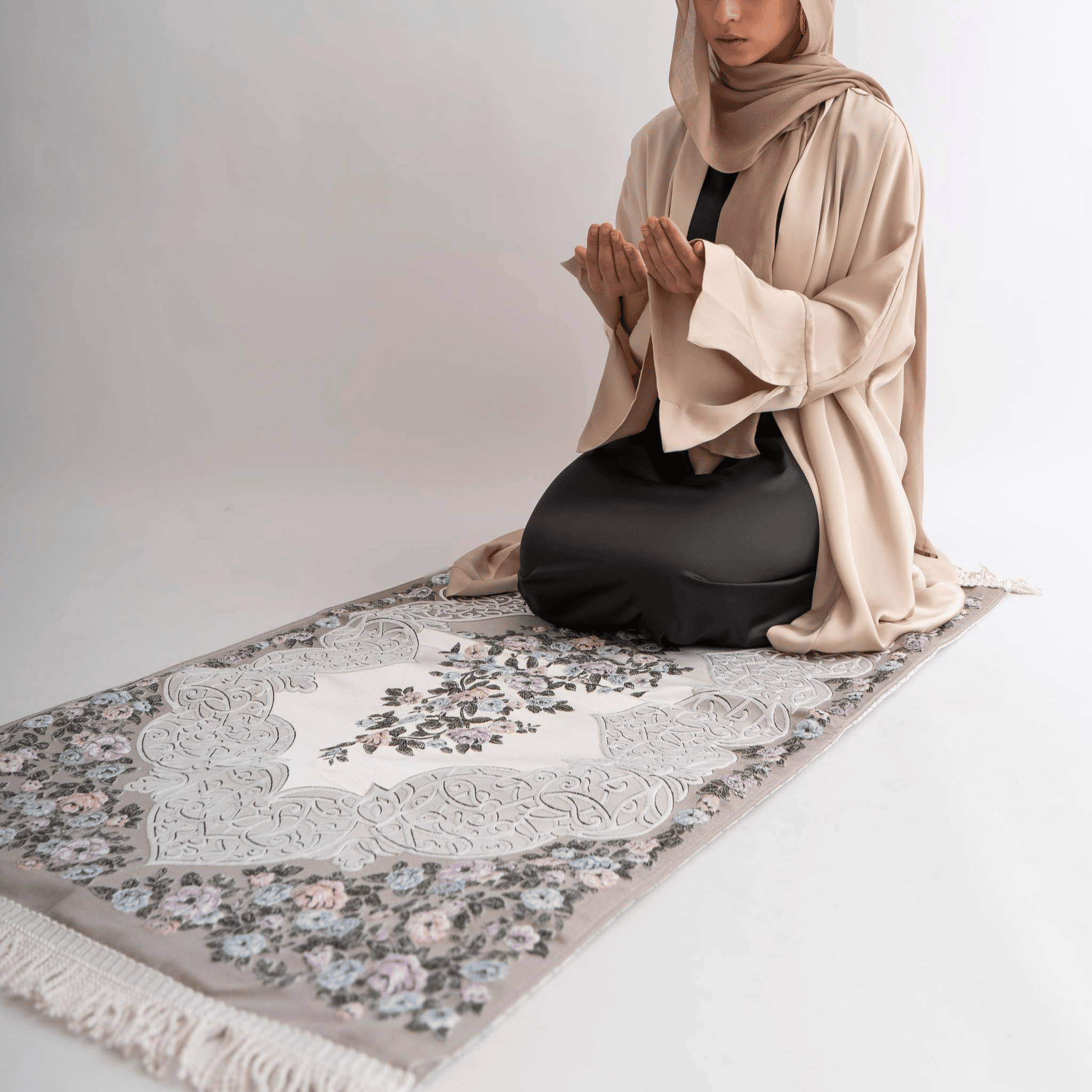 Person sitting on a floral-patterned prayer mat with a plain background