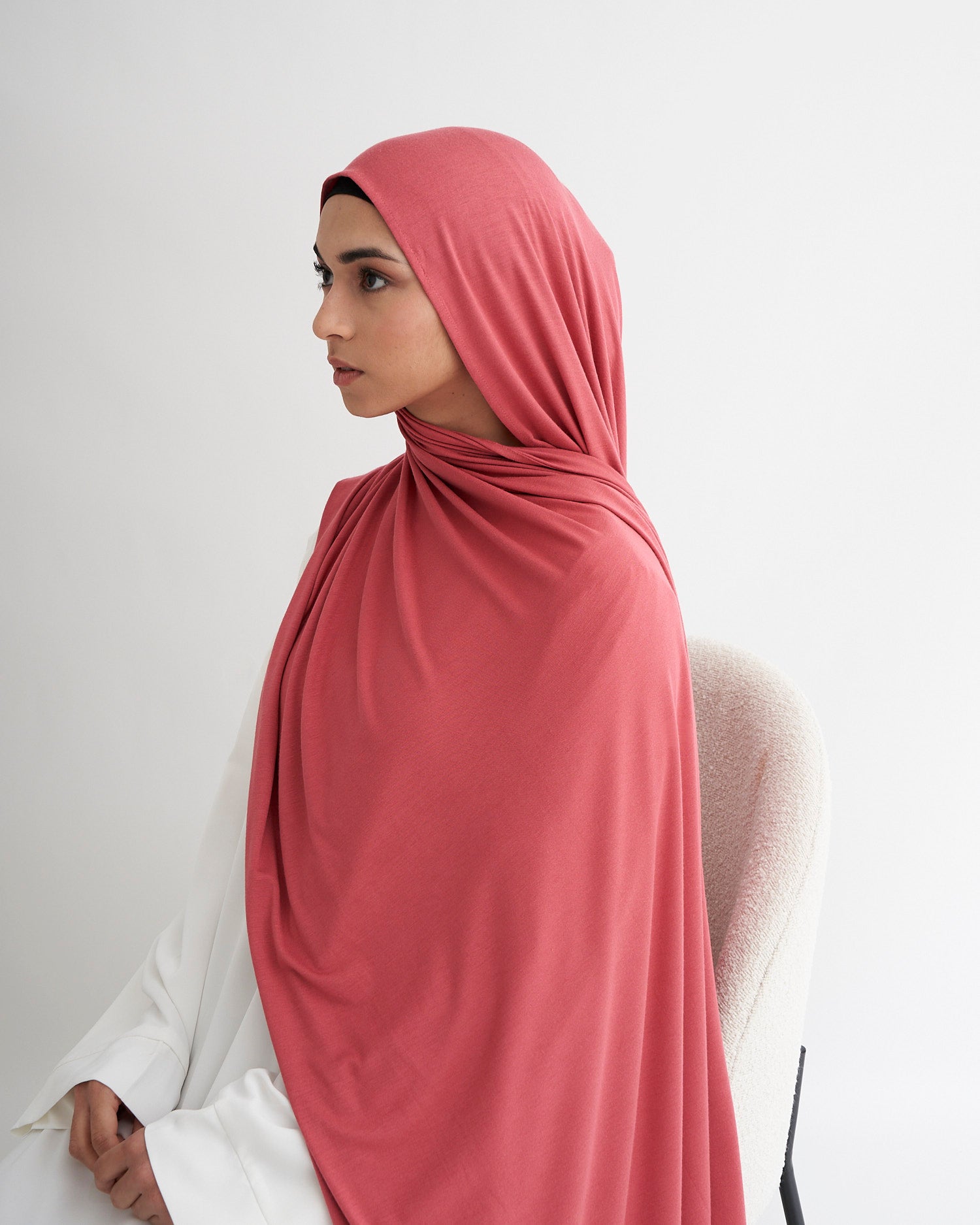 Person wearing a pink hijab and white outfit against a light gray background