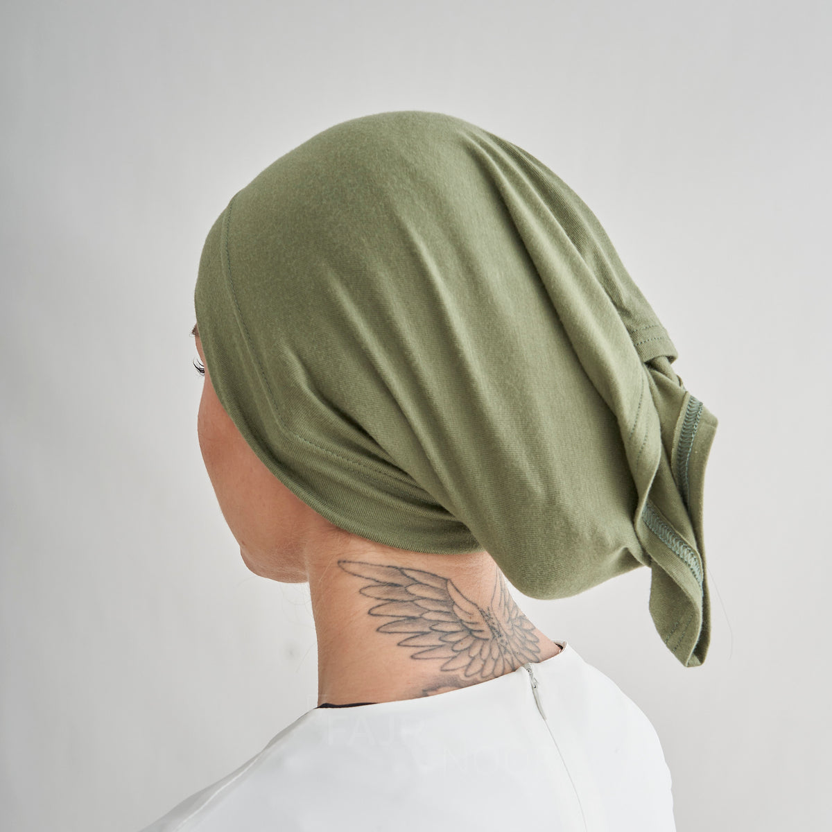 A person shown from the back wearing an olive green fabric head covering or surgical cap, with a tattoo visible on the neck against a plain light gray background.