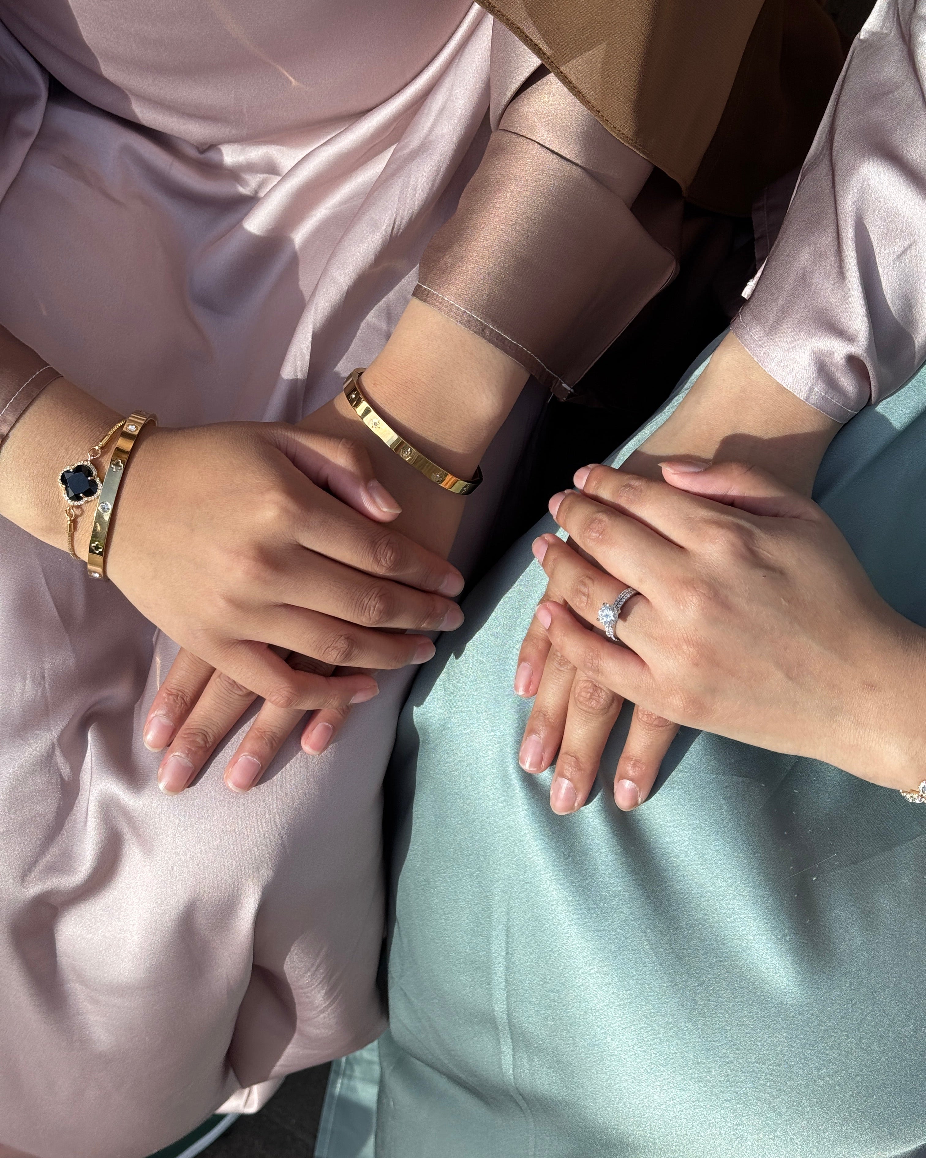 Two pairs of hands with jewelry, one wearing a ring and bracelets on a light background.