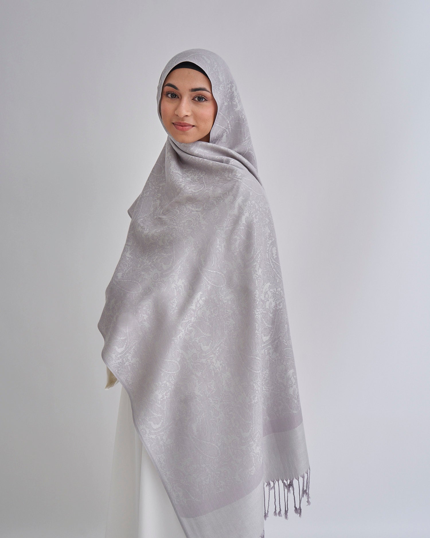 Woman wearing a gray hijab with a subtle pattern on a white background