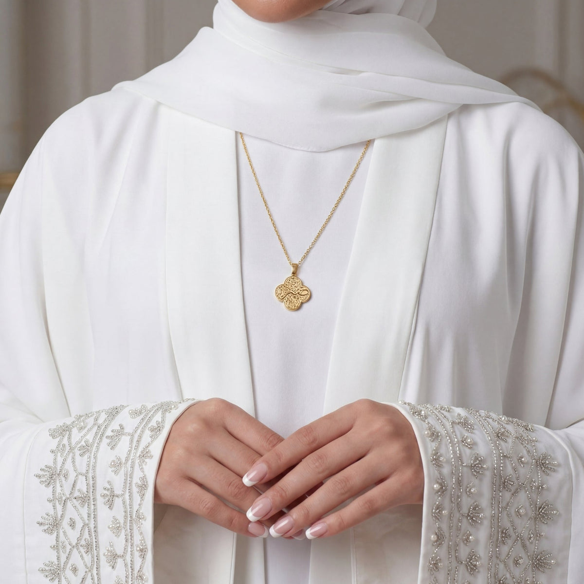 Person wearing a white hijab and embroidered white garment with gold jewelry.