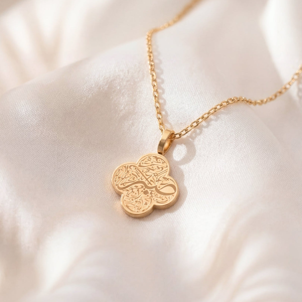 Gold necklace with a clover-shaped pendant on a white fabric background
