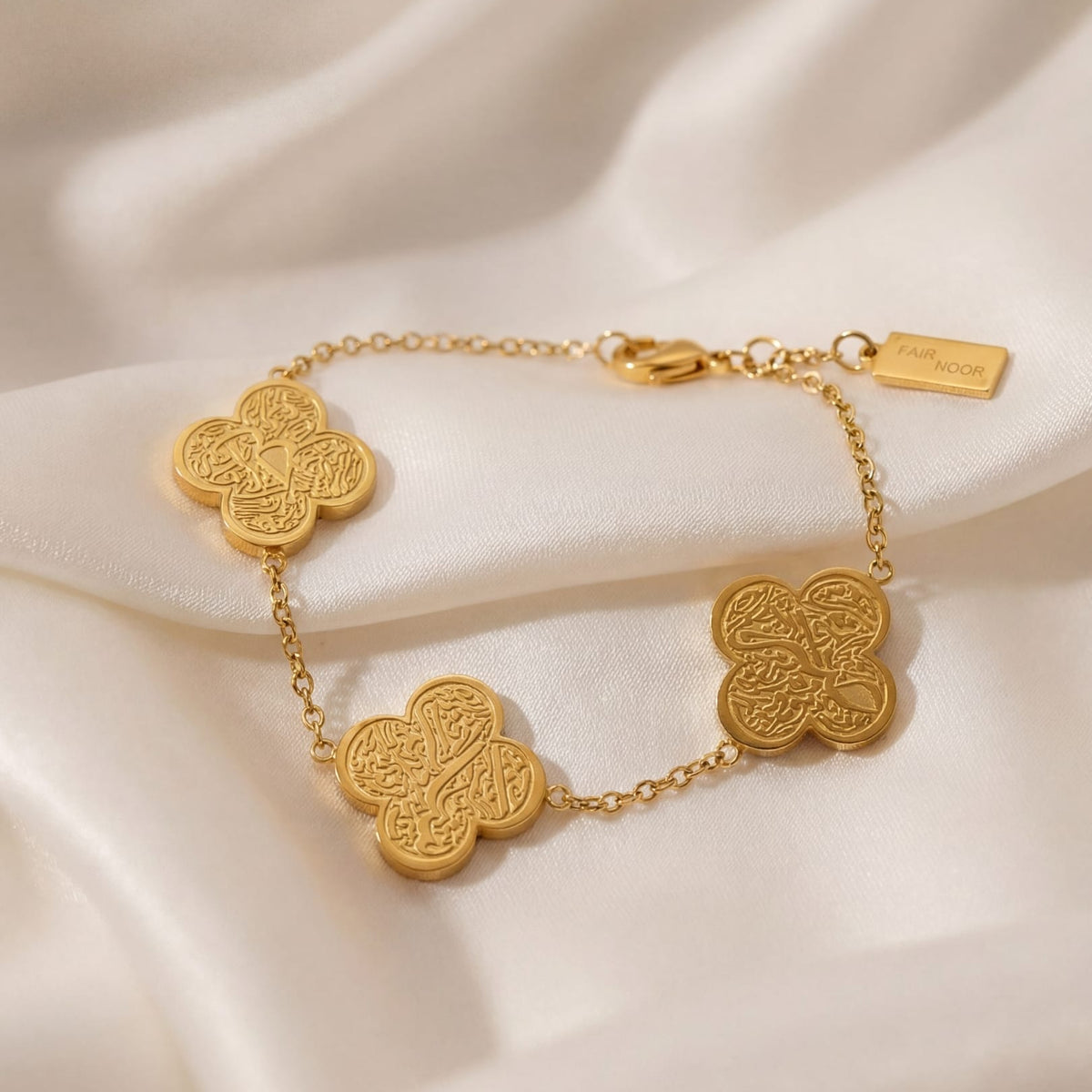 Gold bracelet with clover-shaped links on a beige fabric background