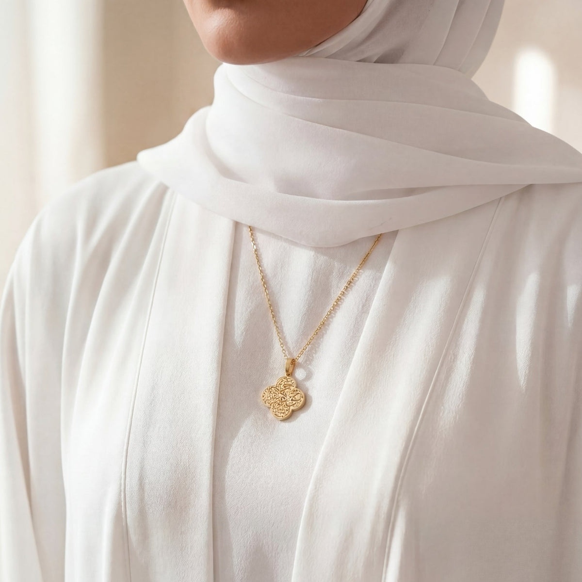 Person wearing a gold necklace with a white hijab