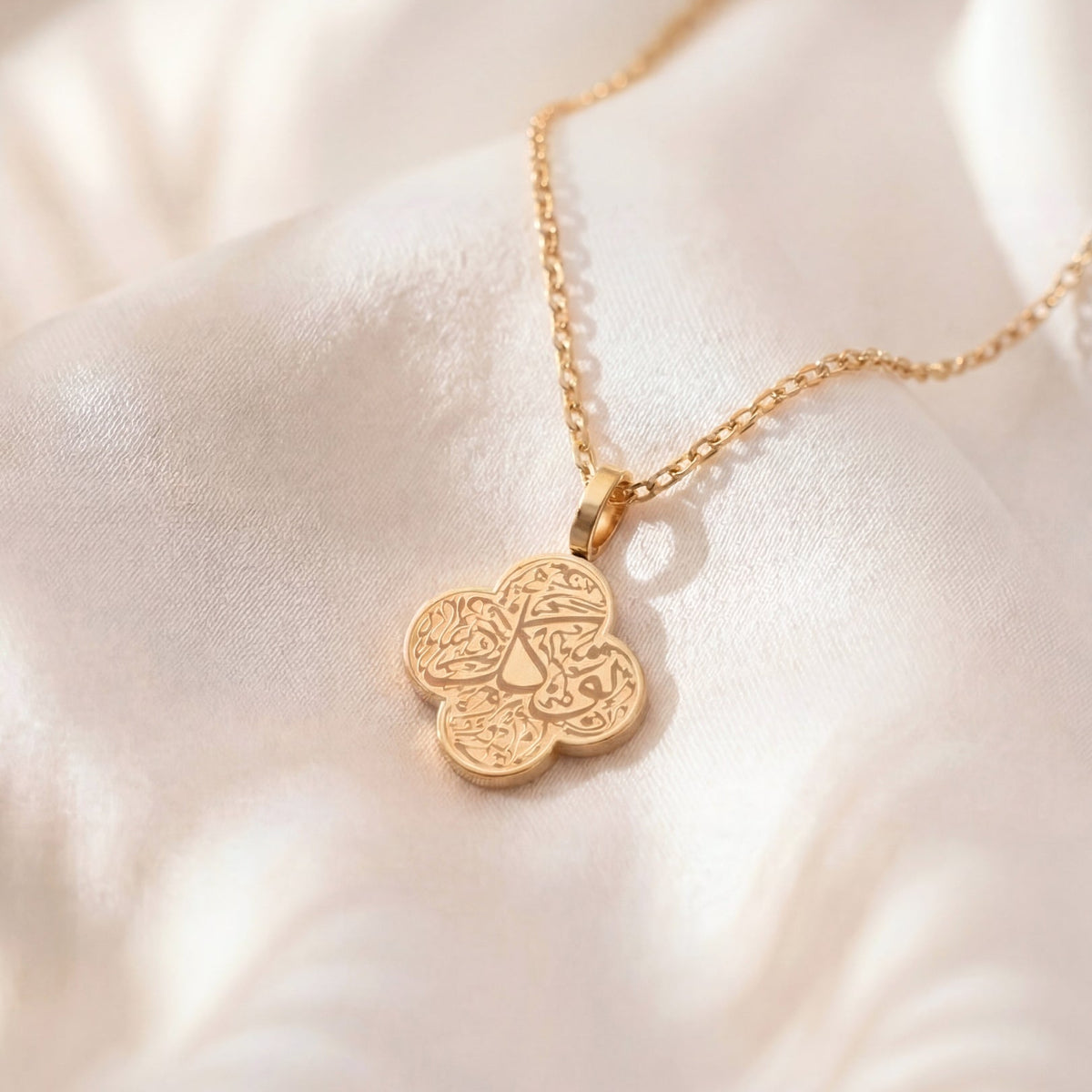 Gold necklace with a floral pendant on a soft white fabric background