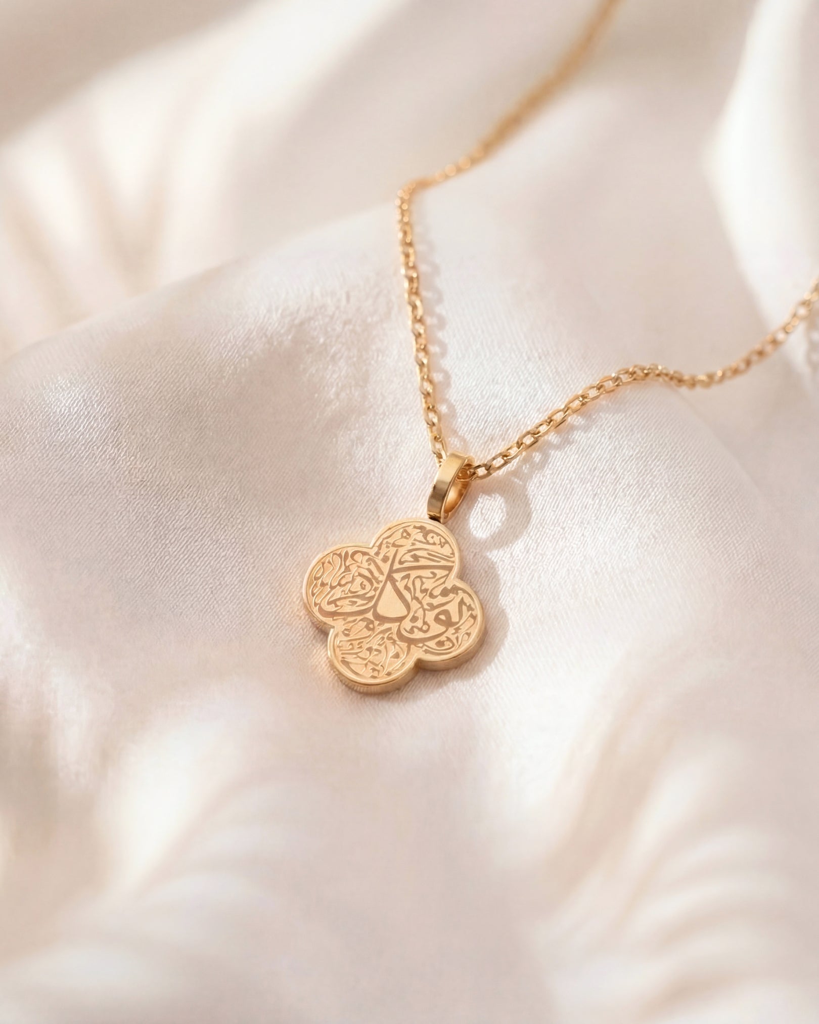 Gold necklace with a floral pendant on a soft white fabric background