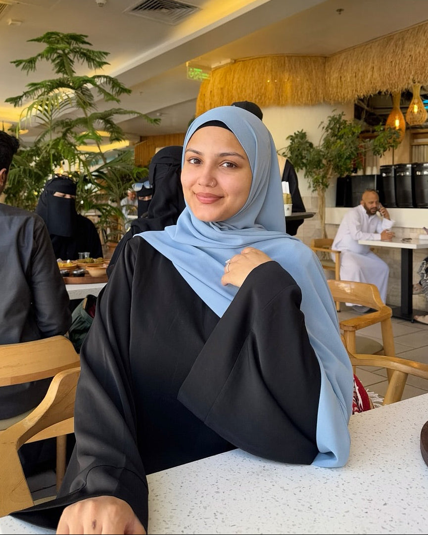 Woman wearing a light blue hijab sitting at a table in a restaurant.