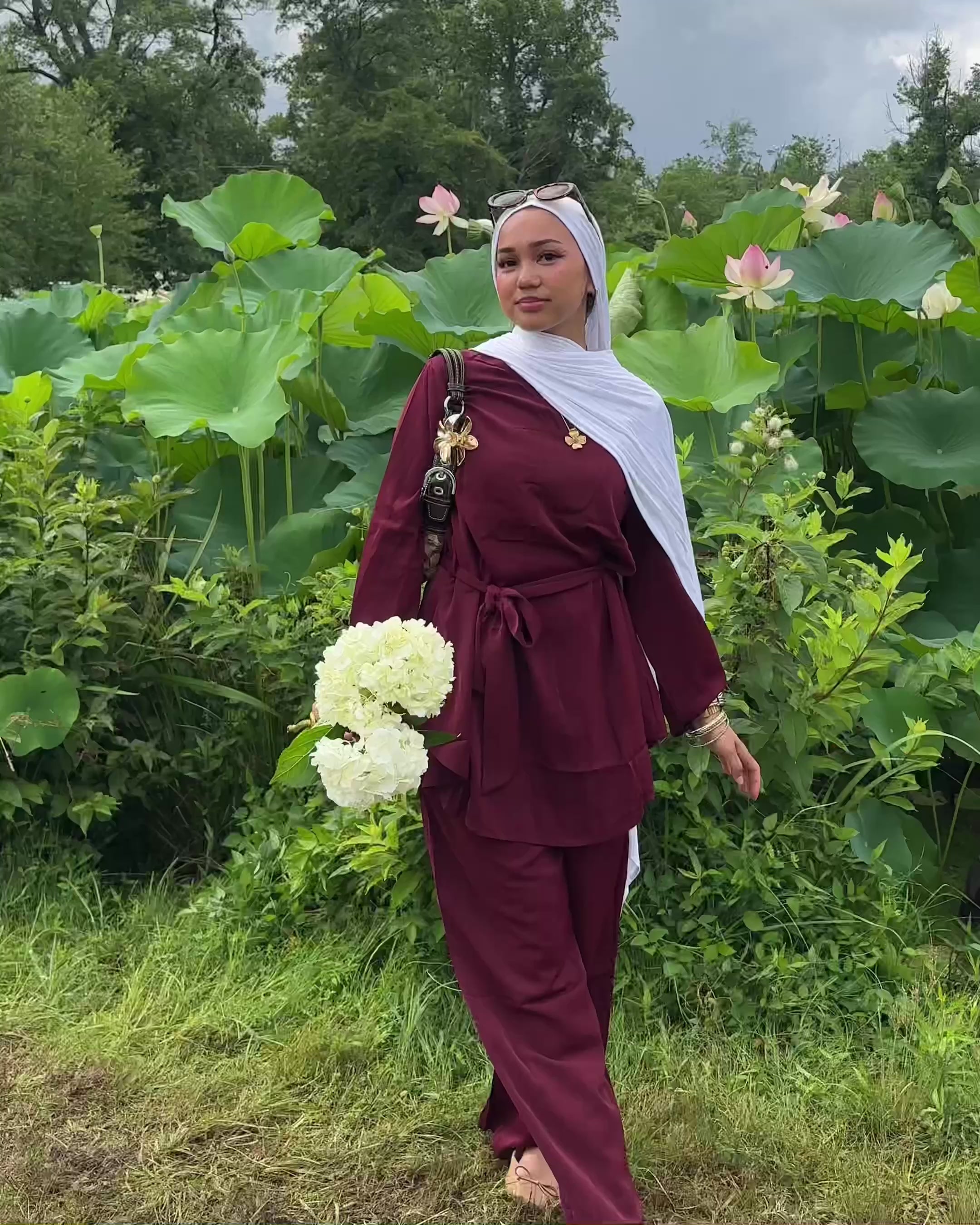 Person wearing a maroon outfit with a hijab against a rainforest.