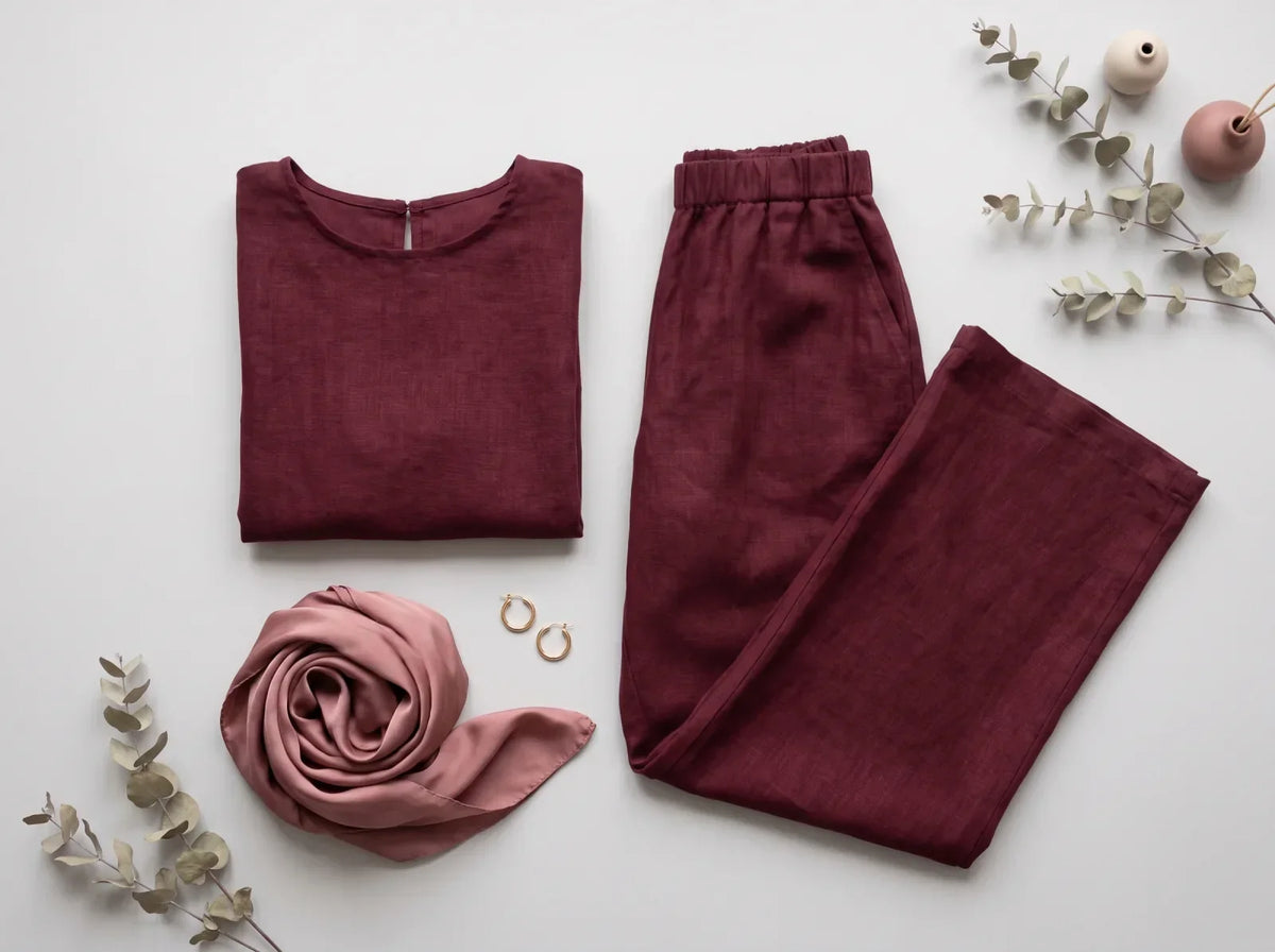 A folded maroon two-piece modest set with a matching satin scarf and gold earrings