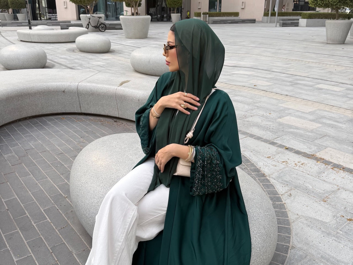 emerald maryam abaya worn in dubai with matching chifon hijab. model wearing sun glasses and clover sabr bracelet with white pants
