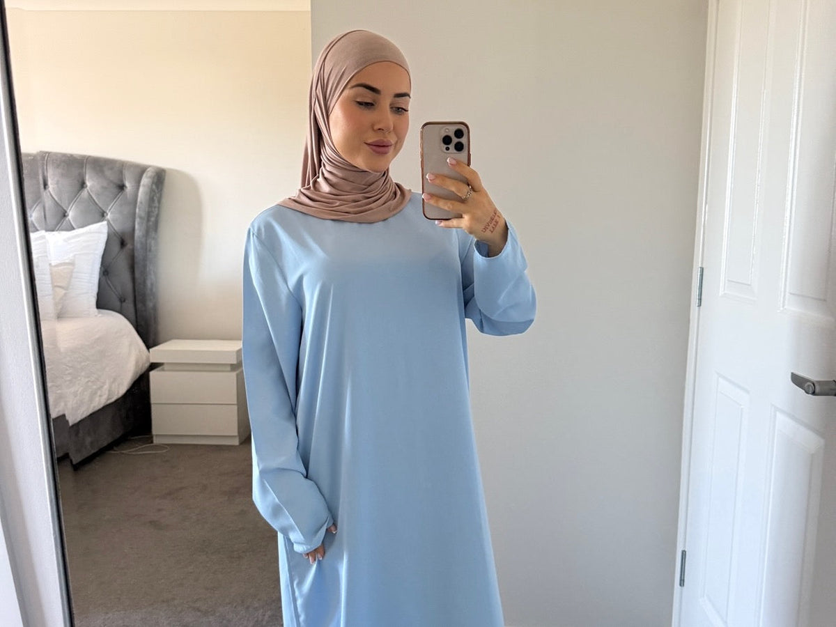 woman wearing hijab and essential sky blue abaya takinga selfie in her bedroom with her iPhone