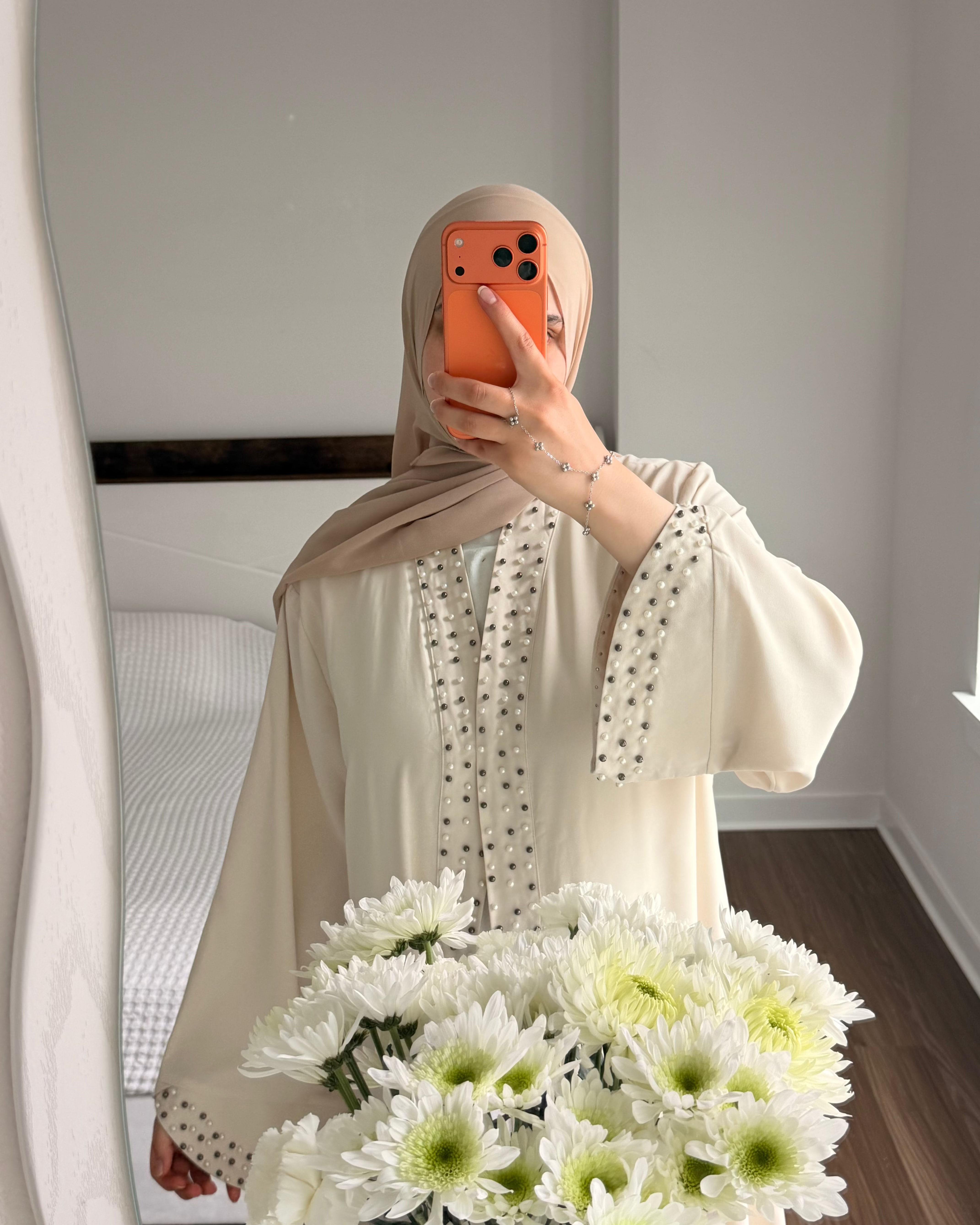 Person holding a bouquet of white flowers in front of a mirror, wearing a beige hijab and light-colored outfit.